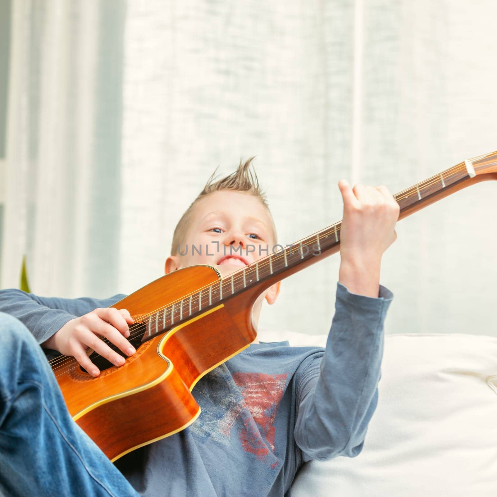 Musical young boy strumming on a guitar at home as he relaxes on a sofa in a close up high key low angle shot