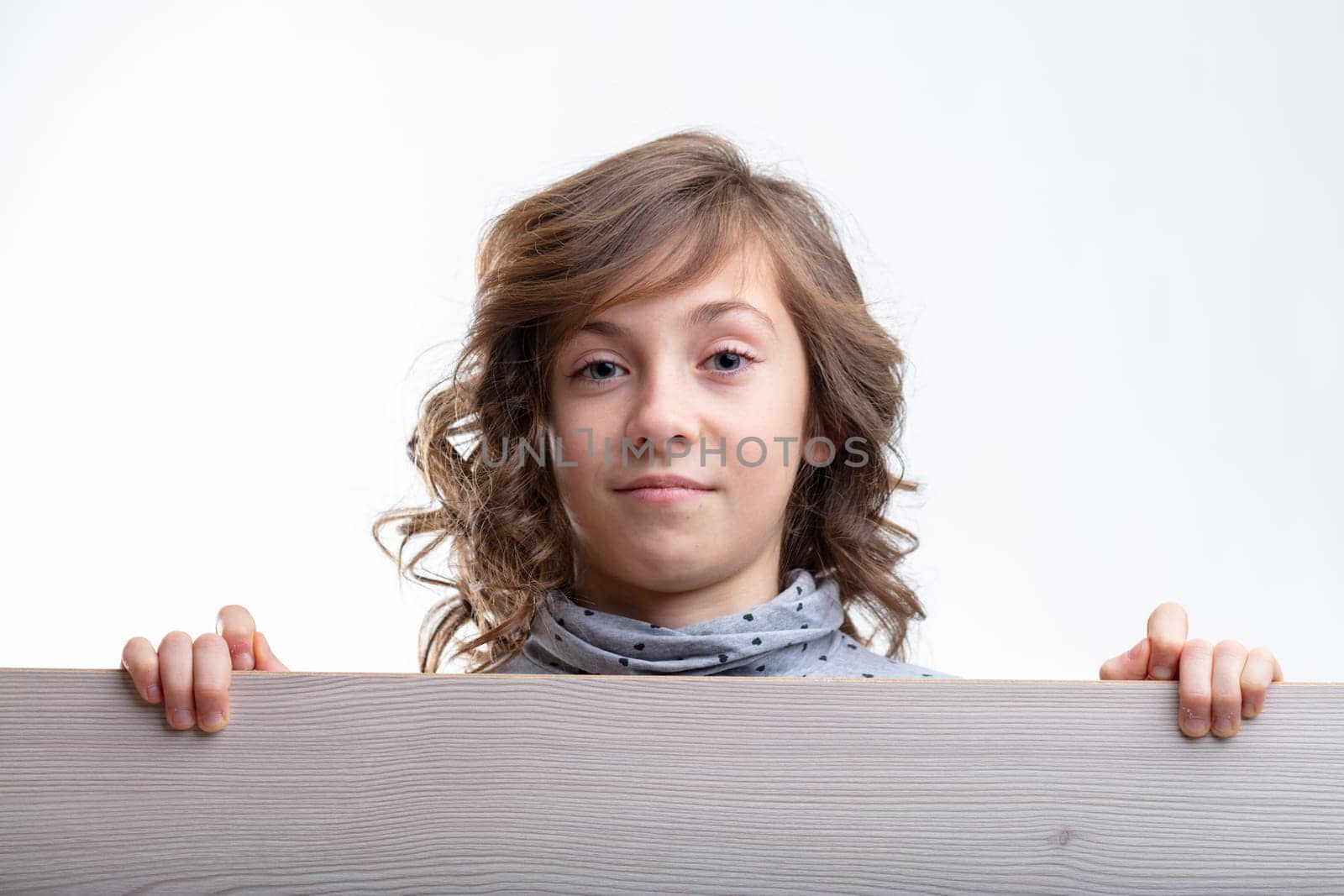 Young girl looking over the top of a wooden board with a quiet smile and thoughtful expression isolated on white