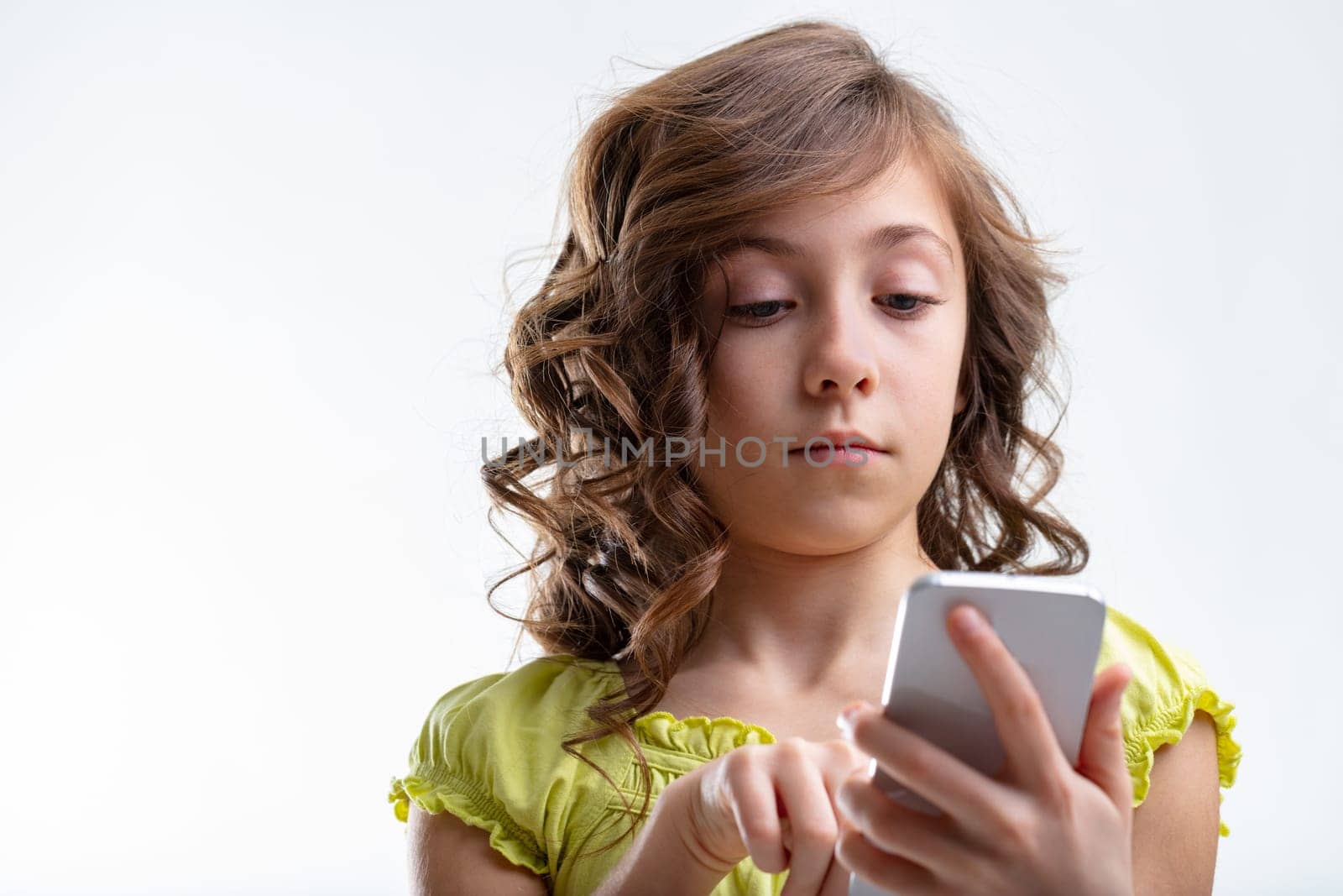 Young girl texting a message on her mobile phone with a look of absorbed concentration in a low angle close up on white