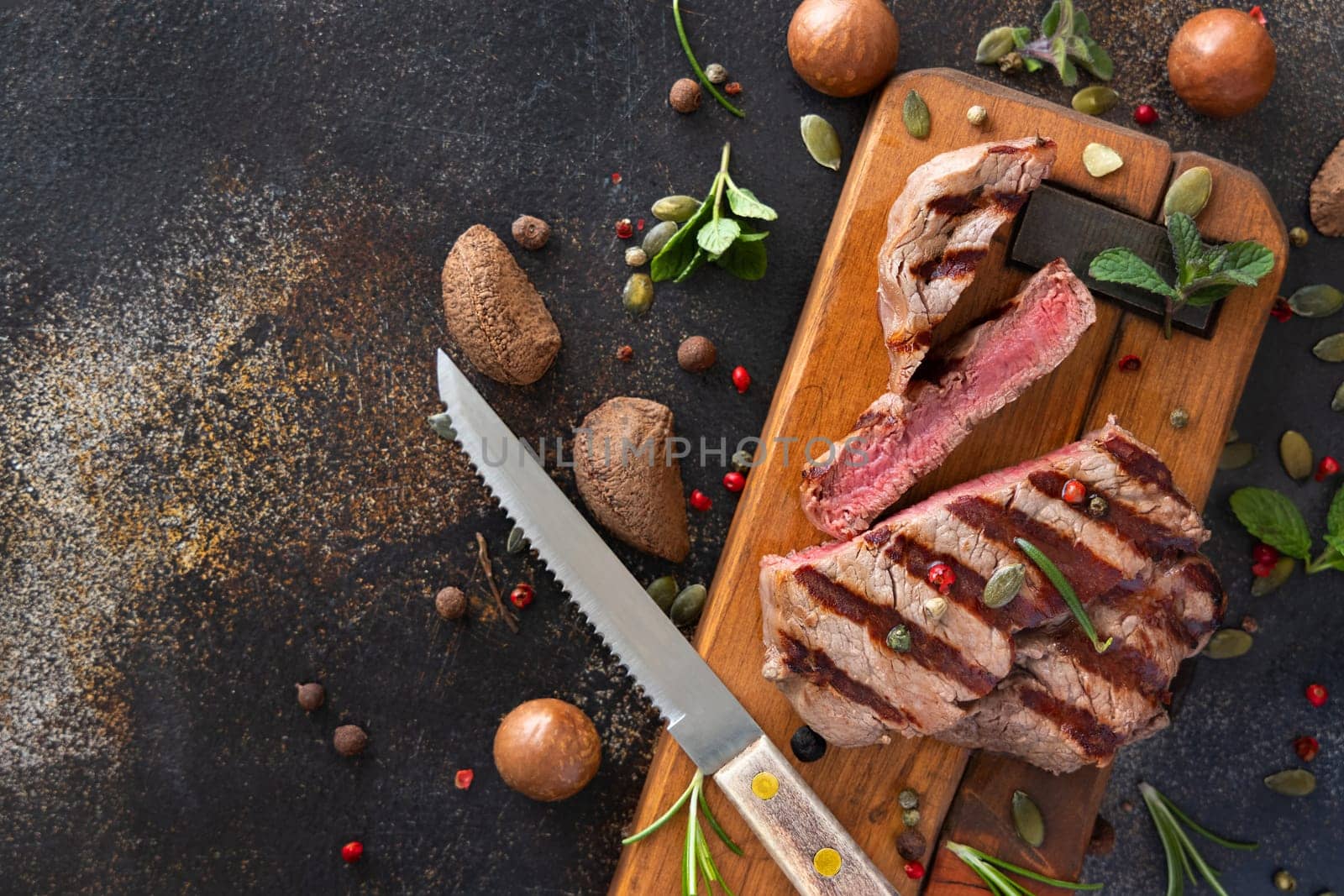 Grilled beef fillet steaks on dark table close up top view. Portioned filet mignon with spices and herbs. Concept of summer food, meat eaters.