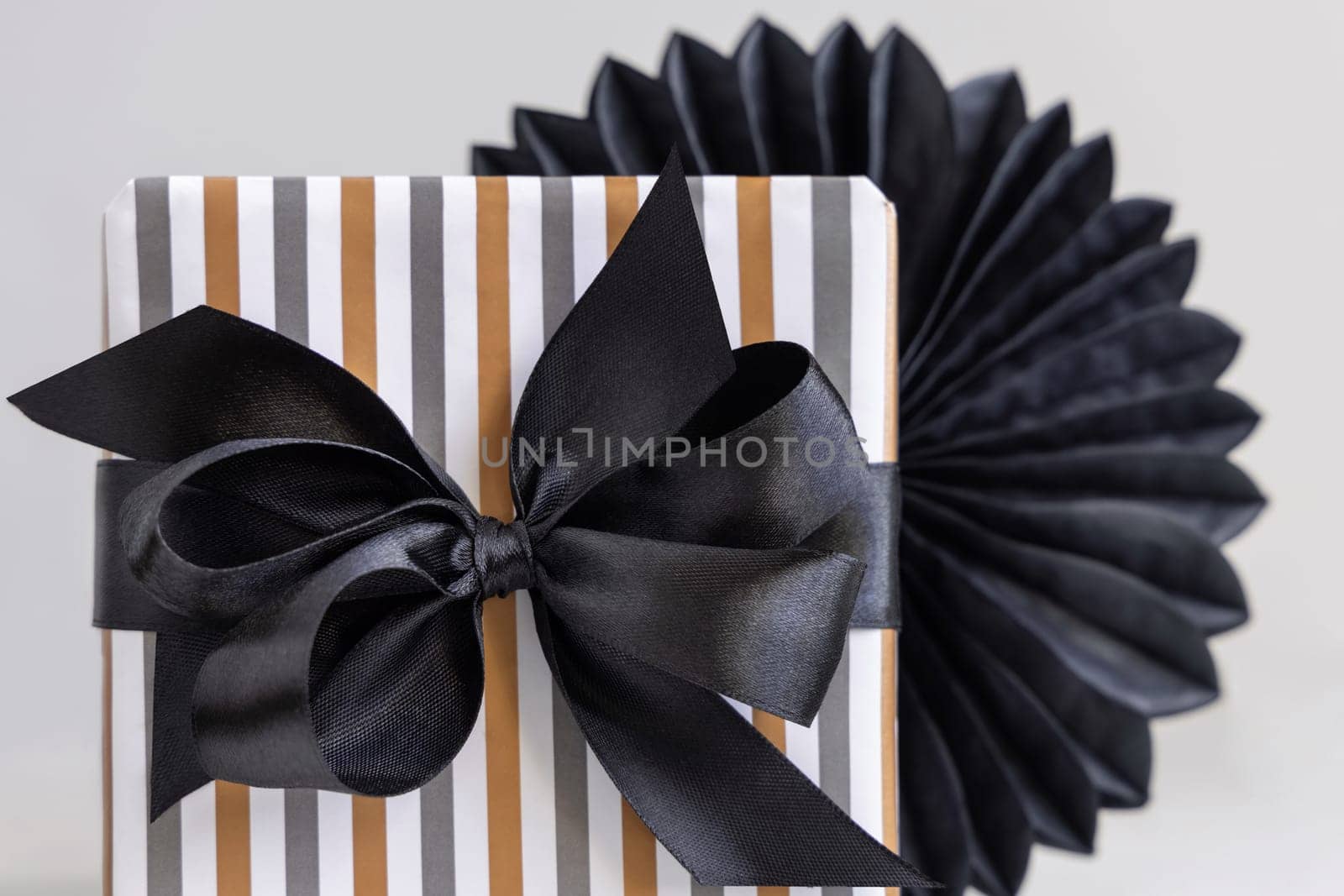 Gift box wrapped in Striped geometric paper with black ribbon bow close up. Christmas, New Year, Birthday, Anniversary concept