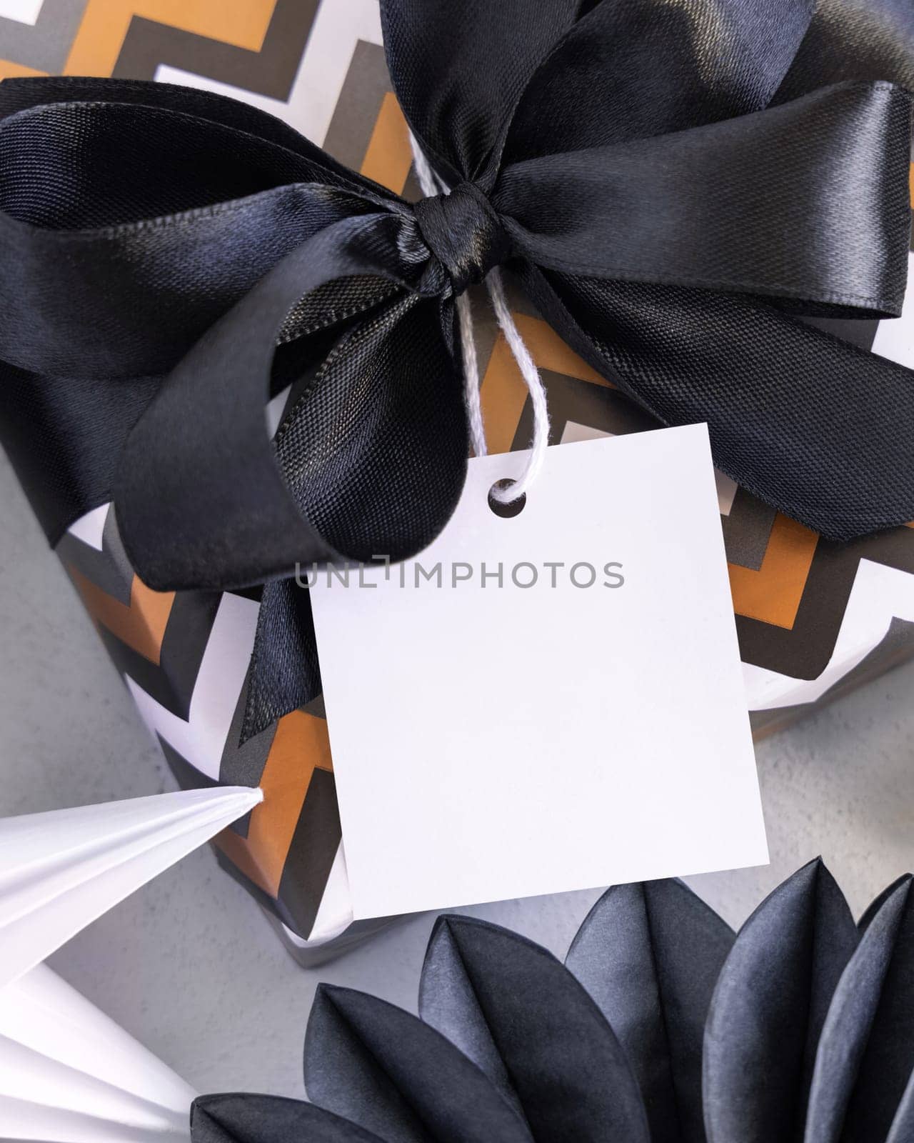 Present with blank square gift tag and black bow close up. Gift boxes wrapped in chevron geometric paper near black and white decor. Christmas, New Year, Birthday, Anniversary label mockup