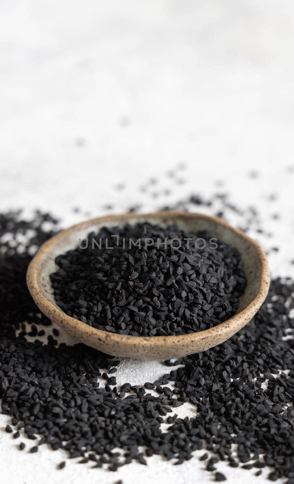 Indian spice Black cumin (nigella sativa or kalonji) seeds in bowl on grey table close up with copy space. Traditional medicine, healthy and vegetarian food concept.