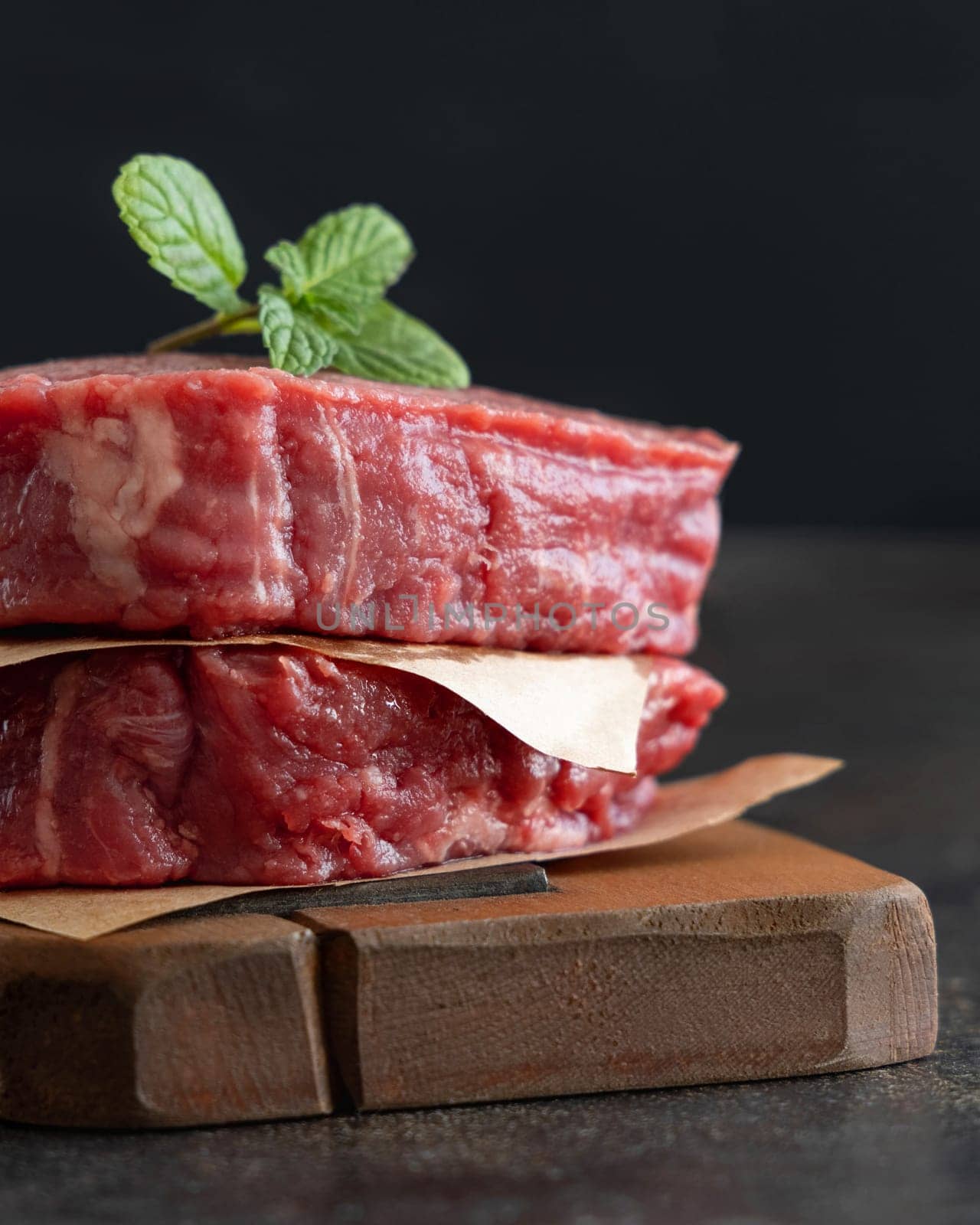 Raw beef fillet steaks on wooden board on dark background close up. Portioned filet mignons with spices and ingredients. Concept of summer food