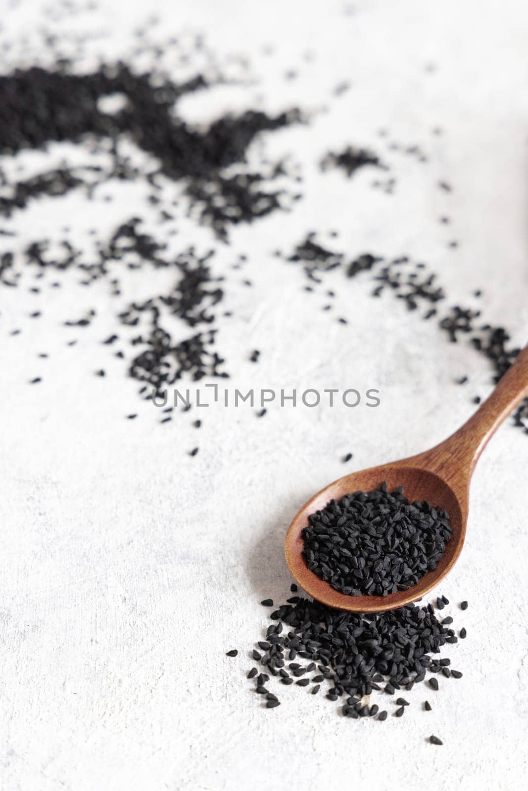 Wooden spoon of Indian spice Black cumin (nigella sativa or kalonji) seeds close up on white table. Traditional asian medicine, healthy eating, vegetarian and vegan food concept