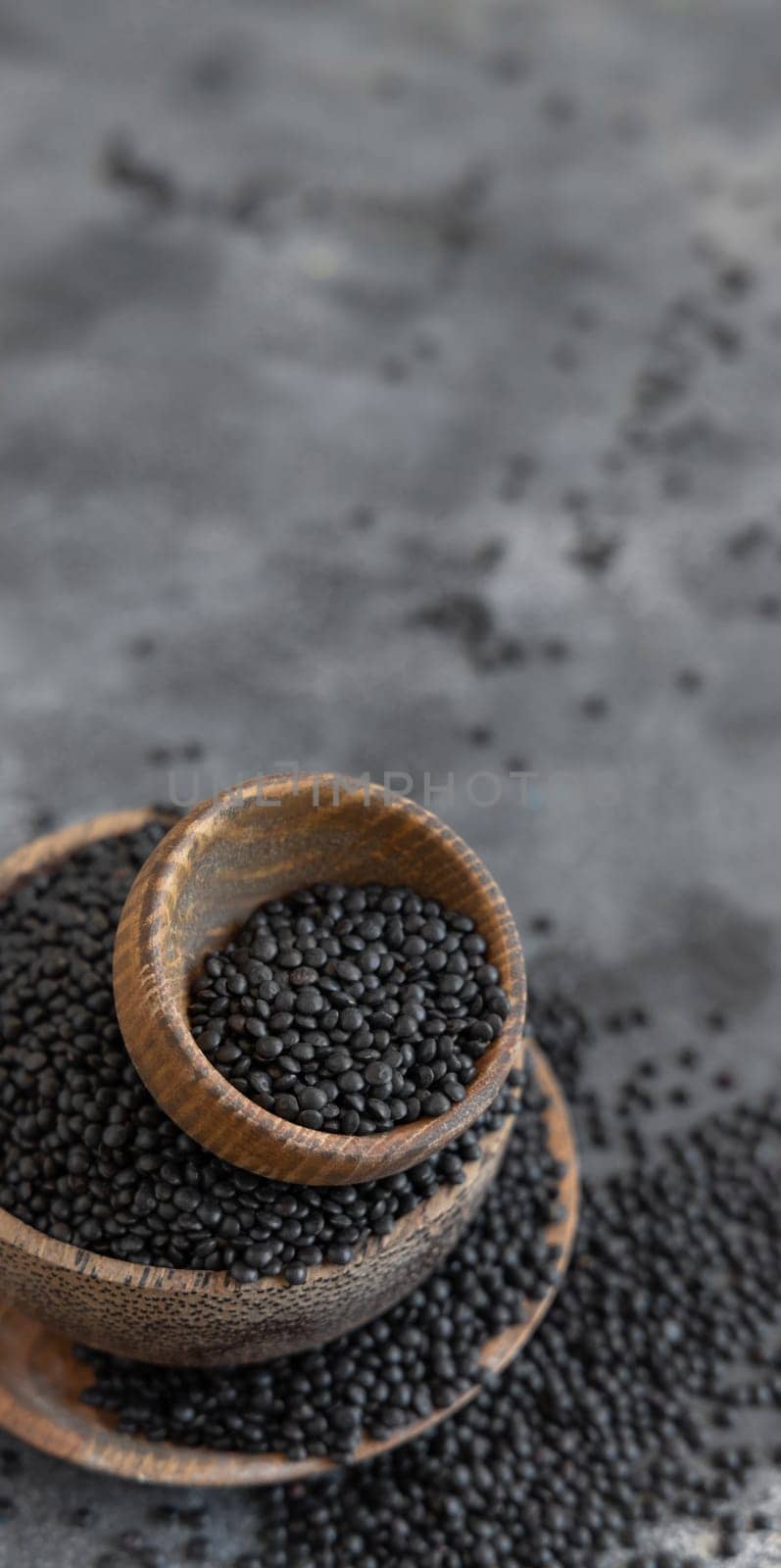 Wooden bowls of black beluga lentils beans on grey table close up. Healthy eating, protein source for vegan and vegetarian diet. Traditional Asian and North African cuisines ingredient