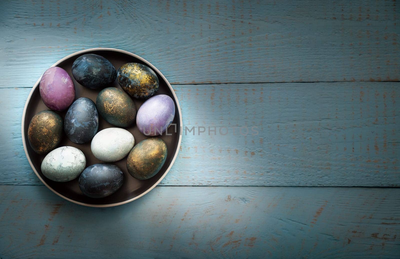 Easter colored eggs in a dish on a blue wooden background. Place for text.
