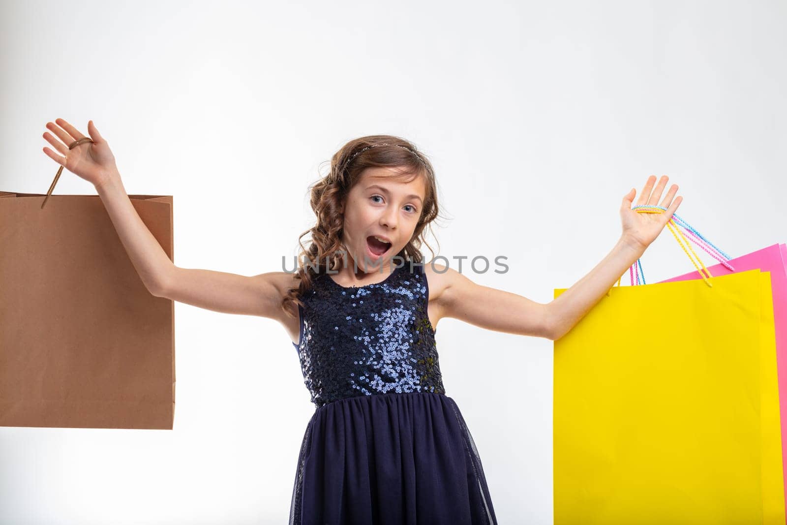 Excited exuberant young girl holding up colorful shopping bags in her hands in a close up three-quarter portrait on white