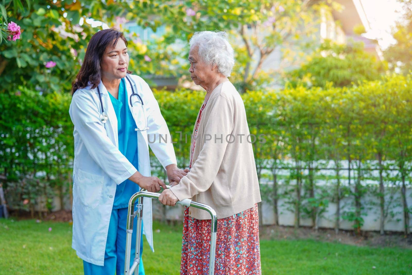 Doctor help Asian elderly woman disability patient walk with walker in park, medical concept.