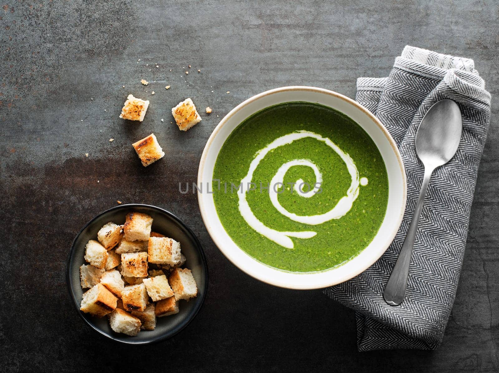 Fresh green soup with cream and croutons on grey background overhead shoot.