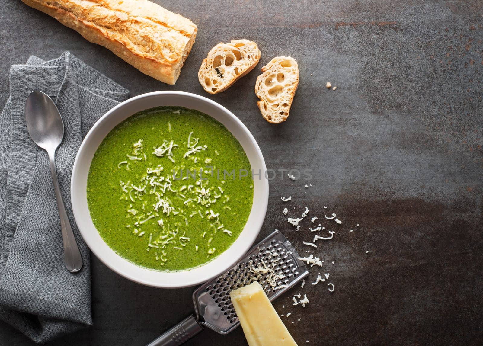 Fresh vegetable cream soup with parmesan cheese on grey background overhead shoot.