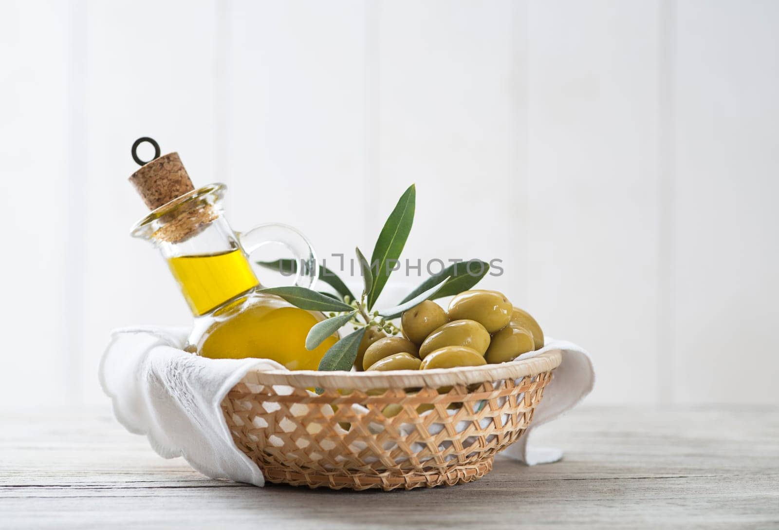 Olive oil bottle and olives with branch leaves in basket on wooden table