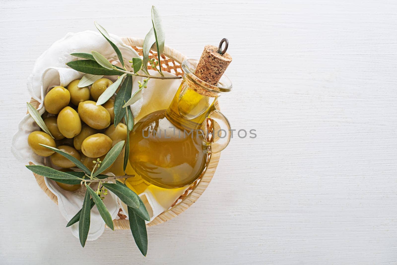 Olive oil bottle and olives with branch in basket on wooden table