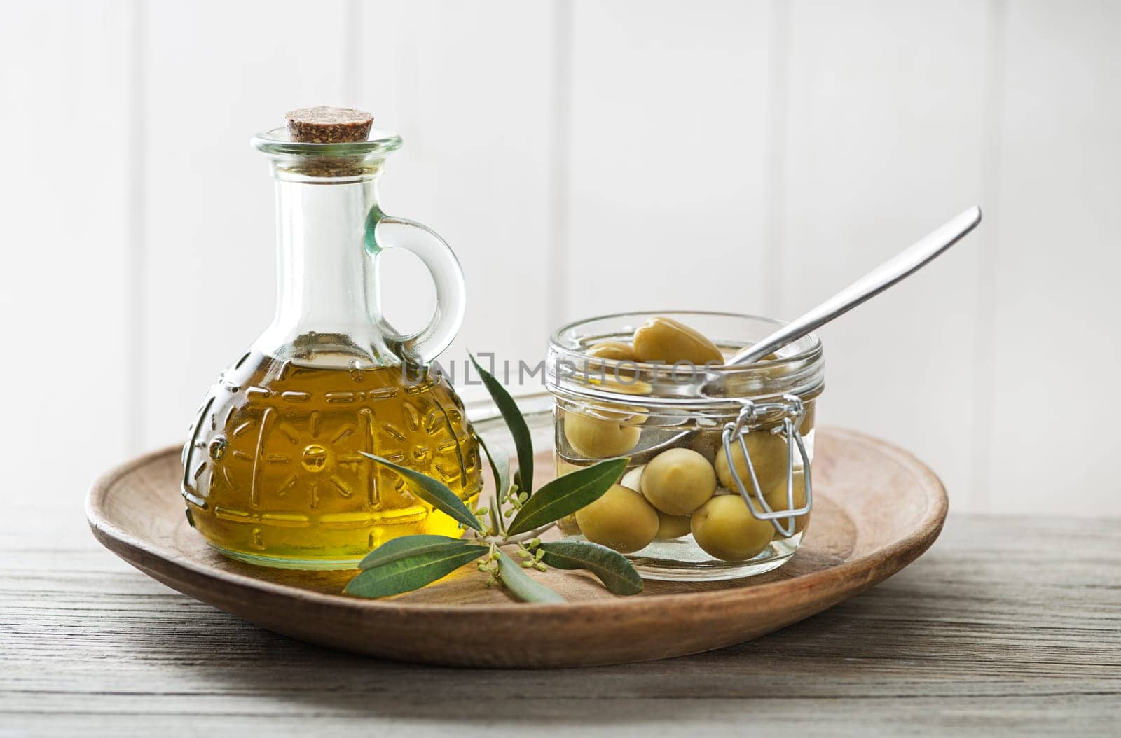 Olive oil bottle and olive branch with Pickled green olives in glass jar on wooden table