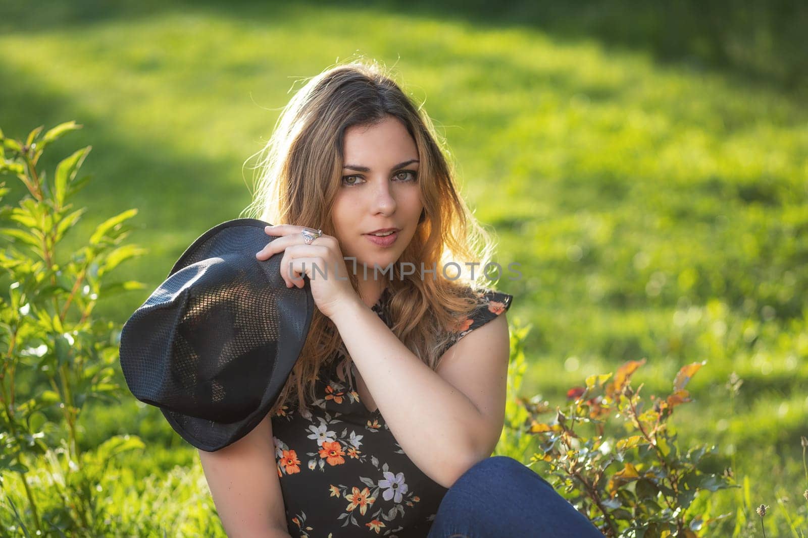 Portrait of attractive  young woman iposing with her black  straw hat outdoors. Horizontally.
