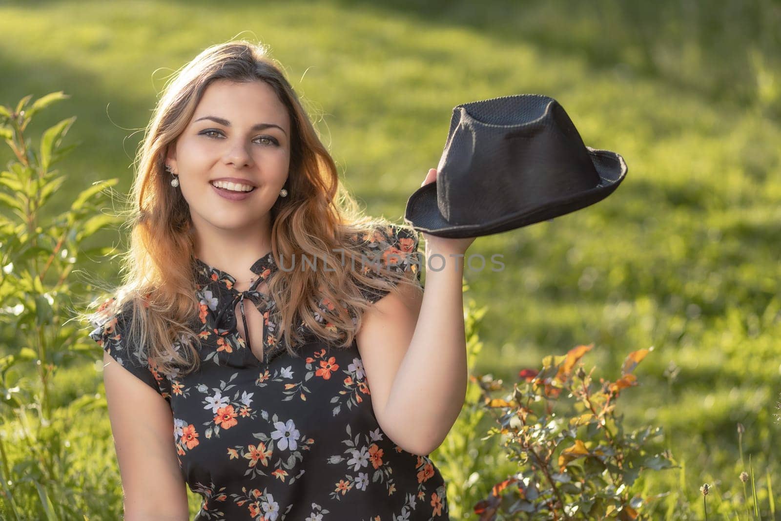 Portrait of smiling attractive  young woman showing her black  straw hat. Horizontally.