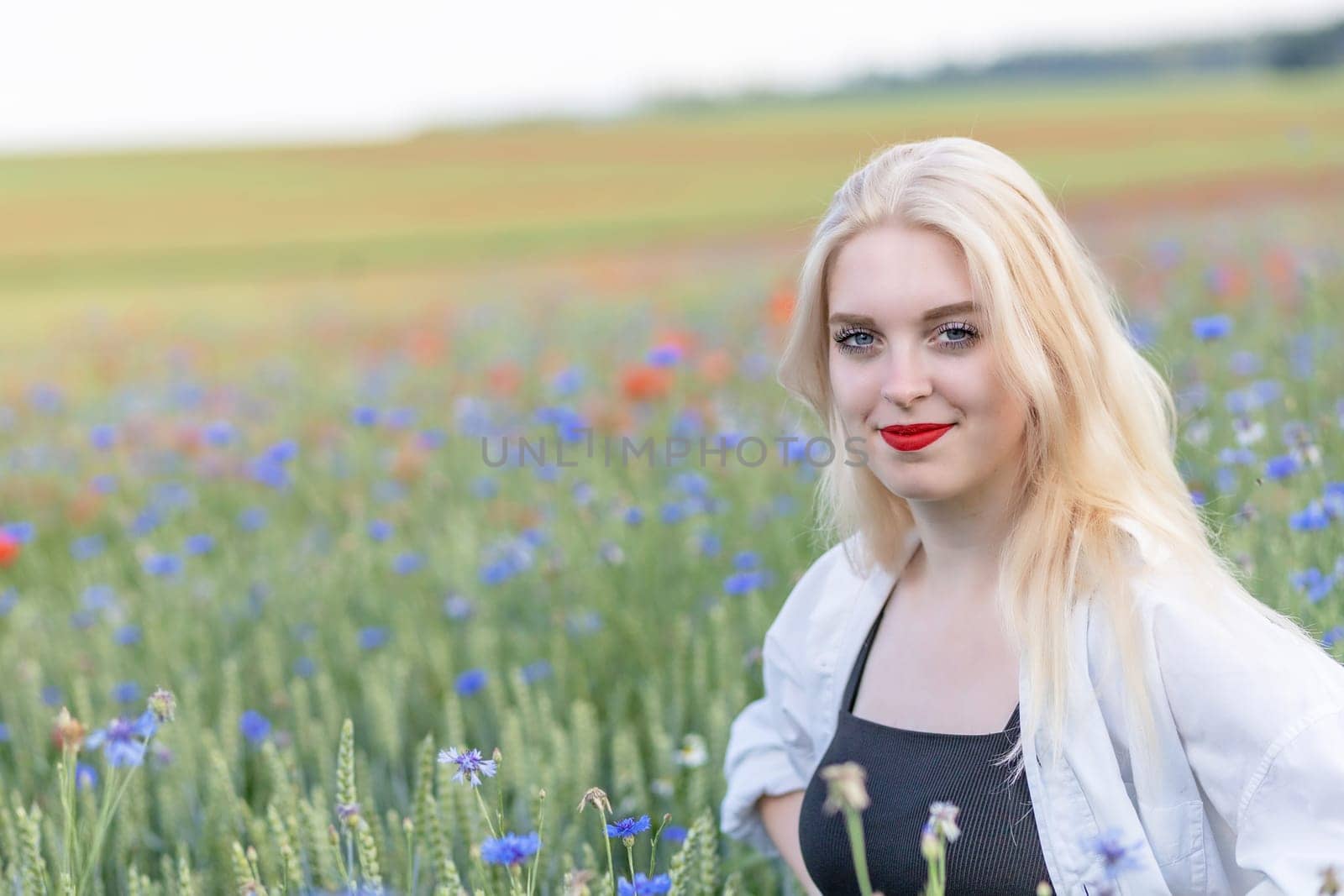 Smiling attractive blonde woman in cornflower and poppy meadow in summer day. Horizontally.