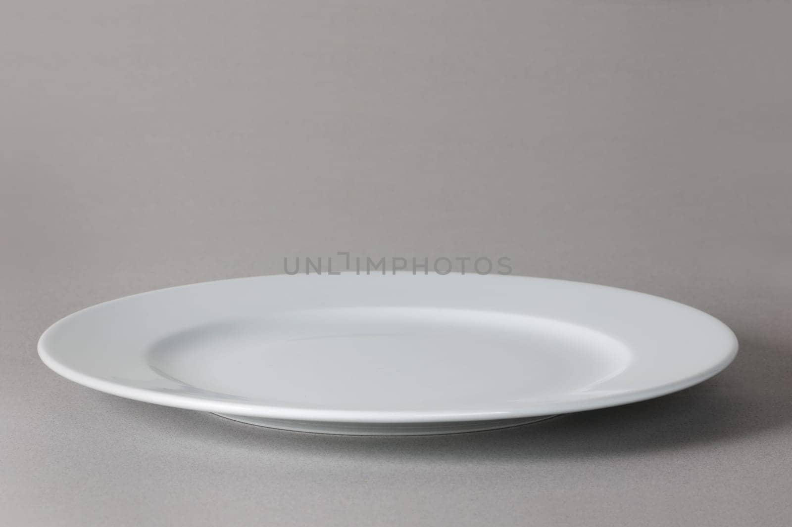 A flat front angle view of a white dinner plate on neutral background with shadow