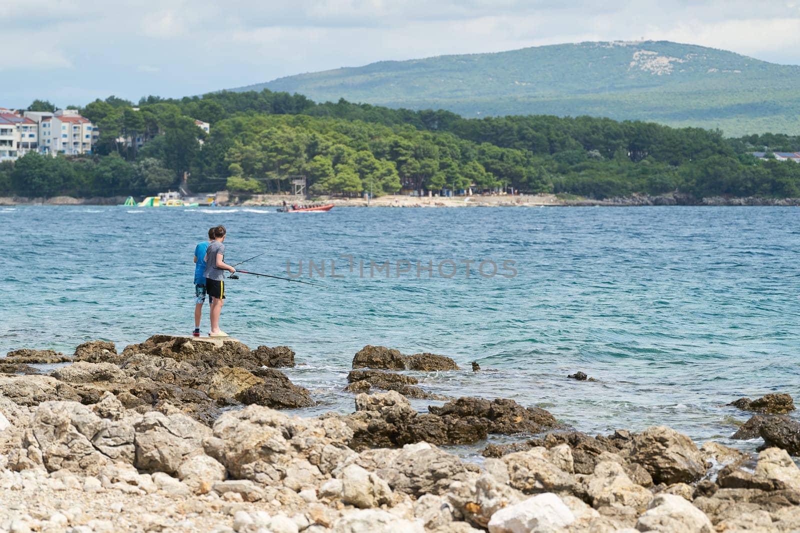 two children standing on rocky coast near town Krk in Croatia fishing