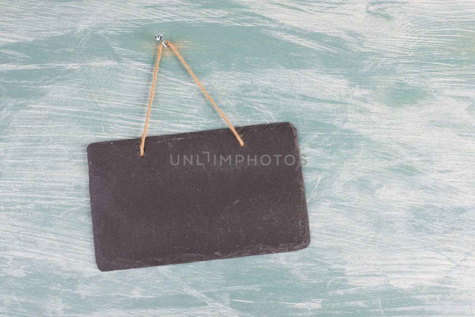 Black chalkboard sign is hanging on a blue textured background, weathered door, welcome and sale concept, copy space for text