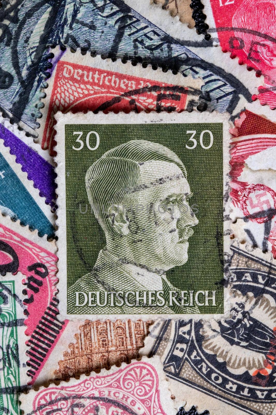 Potsdam, Germany - APR 26, 2022. A stack of old German stamps from the Third Reich and on it a stamp with printed portrait of Adolf Hitler, the leader of NSDAP party. Macro.