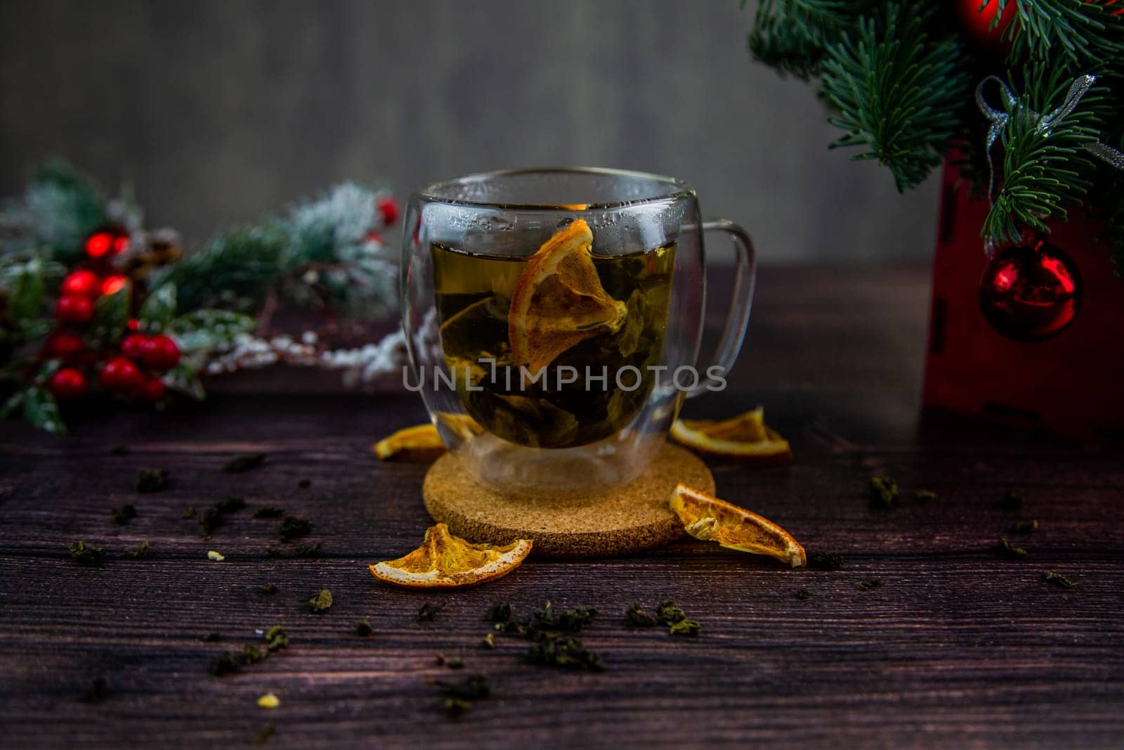 A transparent cup of tea stands on a dark table, on a wooden stand, dried orange slices float in the cup, citrus slices lie next to it, tea is scattered, a photo in a dark key. High quality photo