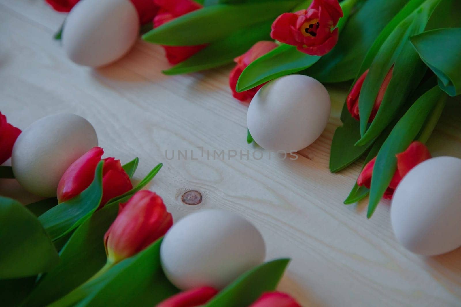 Pink tulips with green leaves lie horizontally mixed with white Easter eggs, leaving free space diagonally. High quality photo