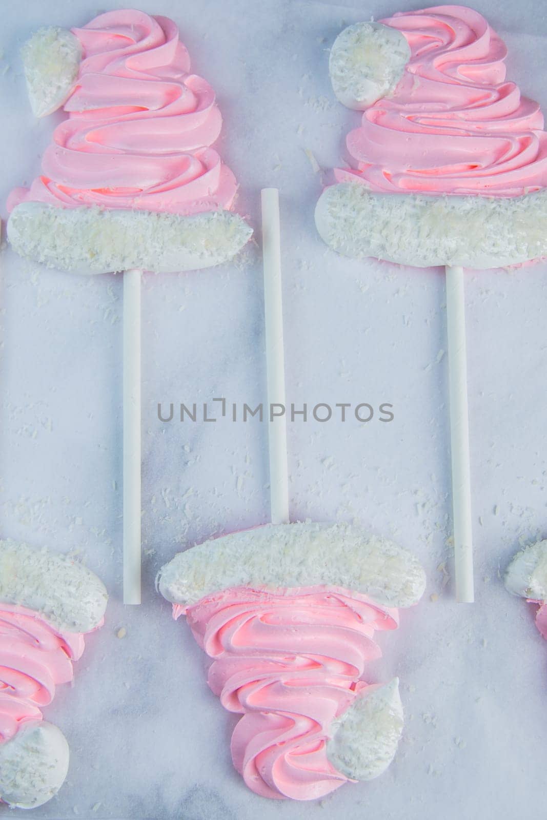 Meringue in the form of pink Christmas hats with a pompom and a white lapel on a stick lie on white parchment in two rows. High quality photo