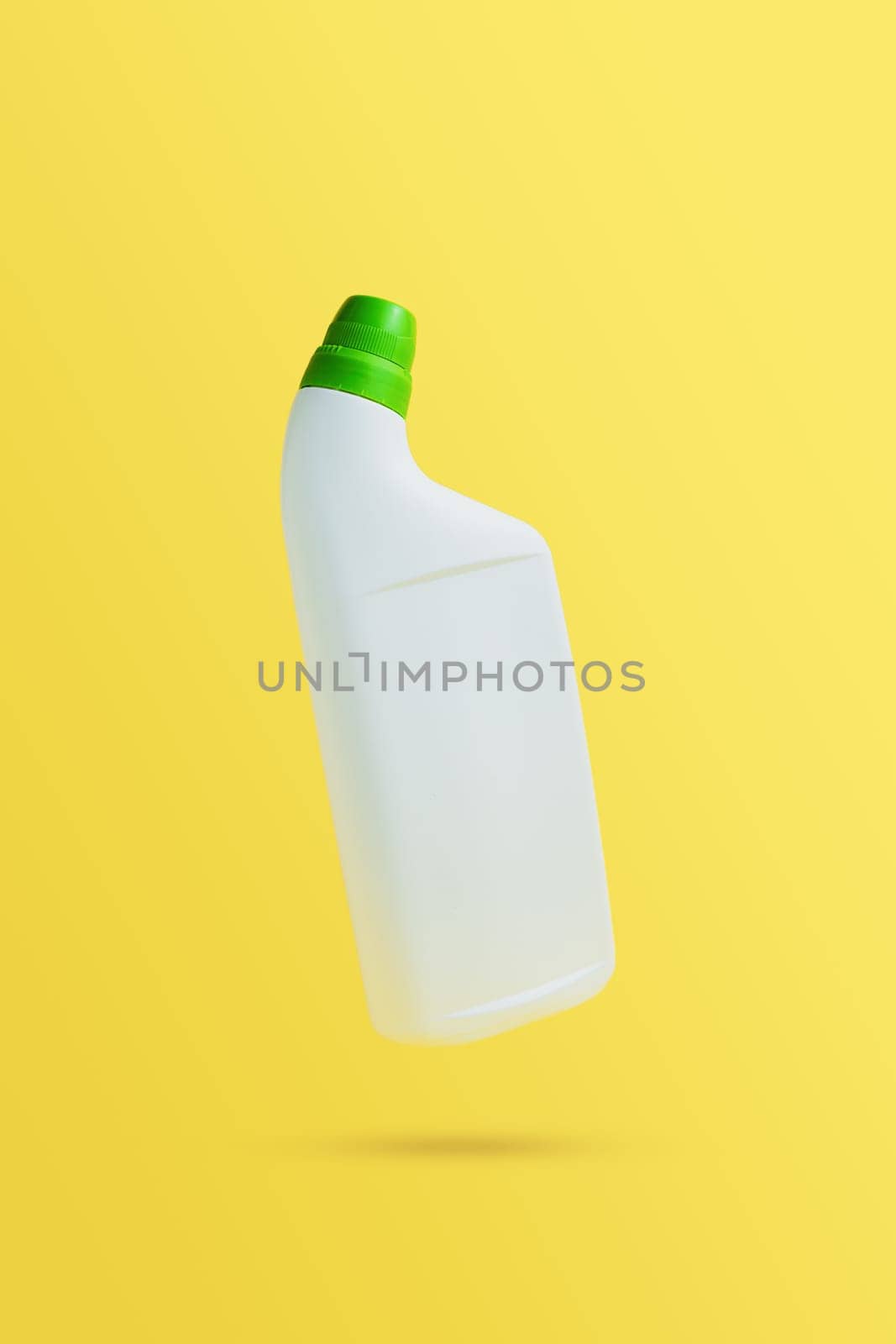 Levitating or flying blank toilet cleaner bottle with green cap. Isolated on yellow background. White plastic packaging. Household chemistry. Front, side view. Falling single object in air with shadow
