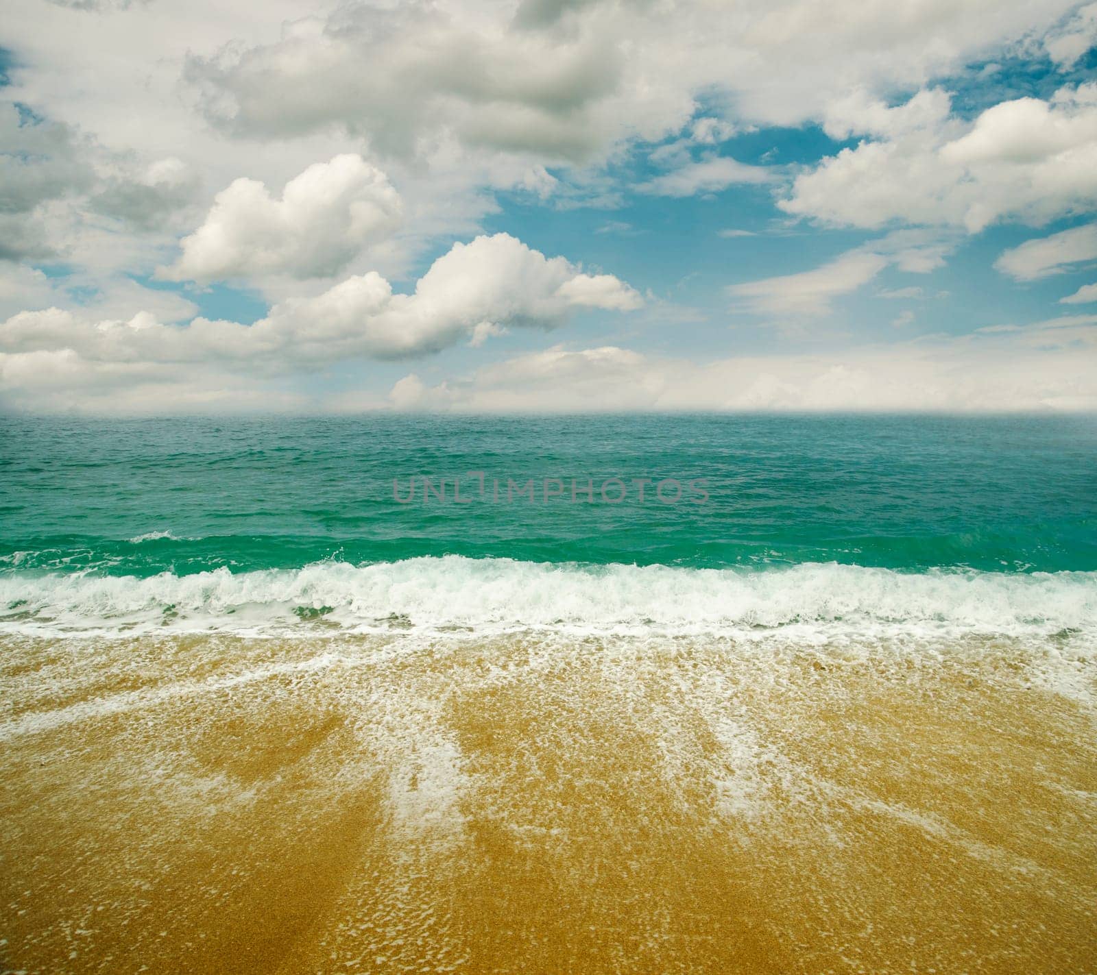 Sandy beach, sea and blue sky with clouds.