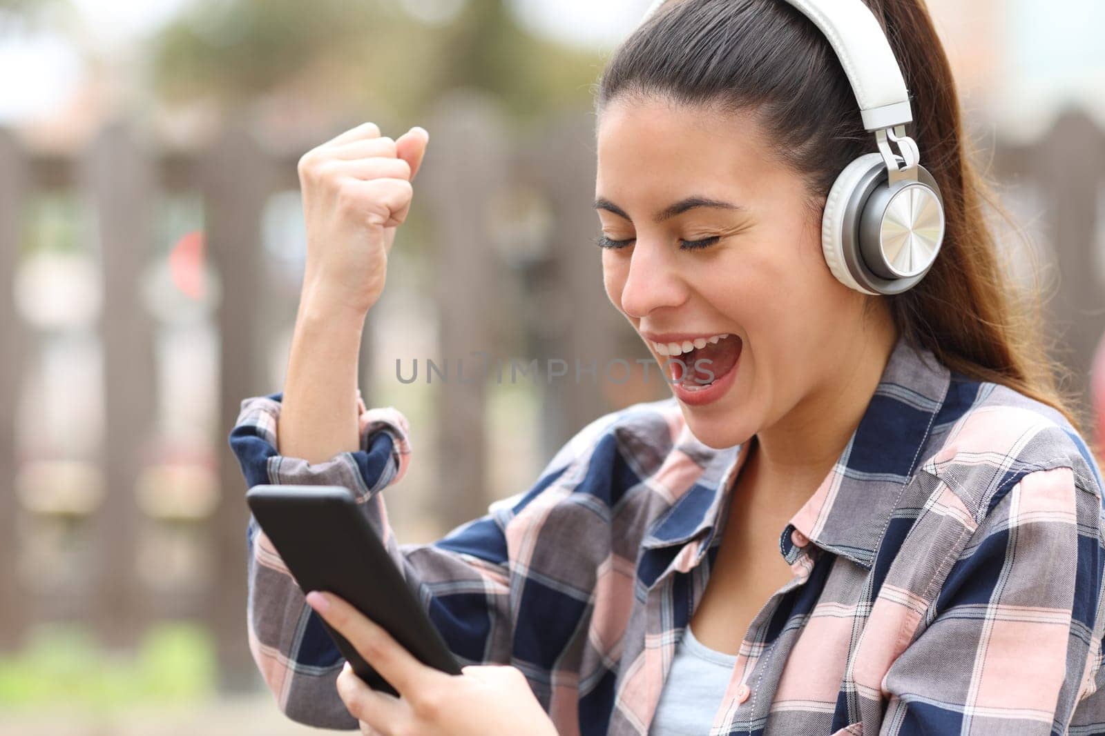 Excited teen with headphones checking smart phone