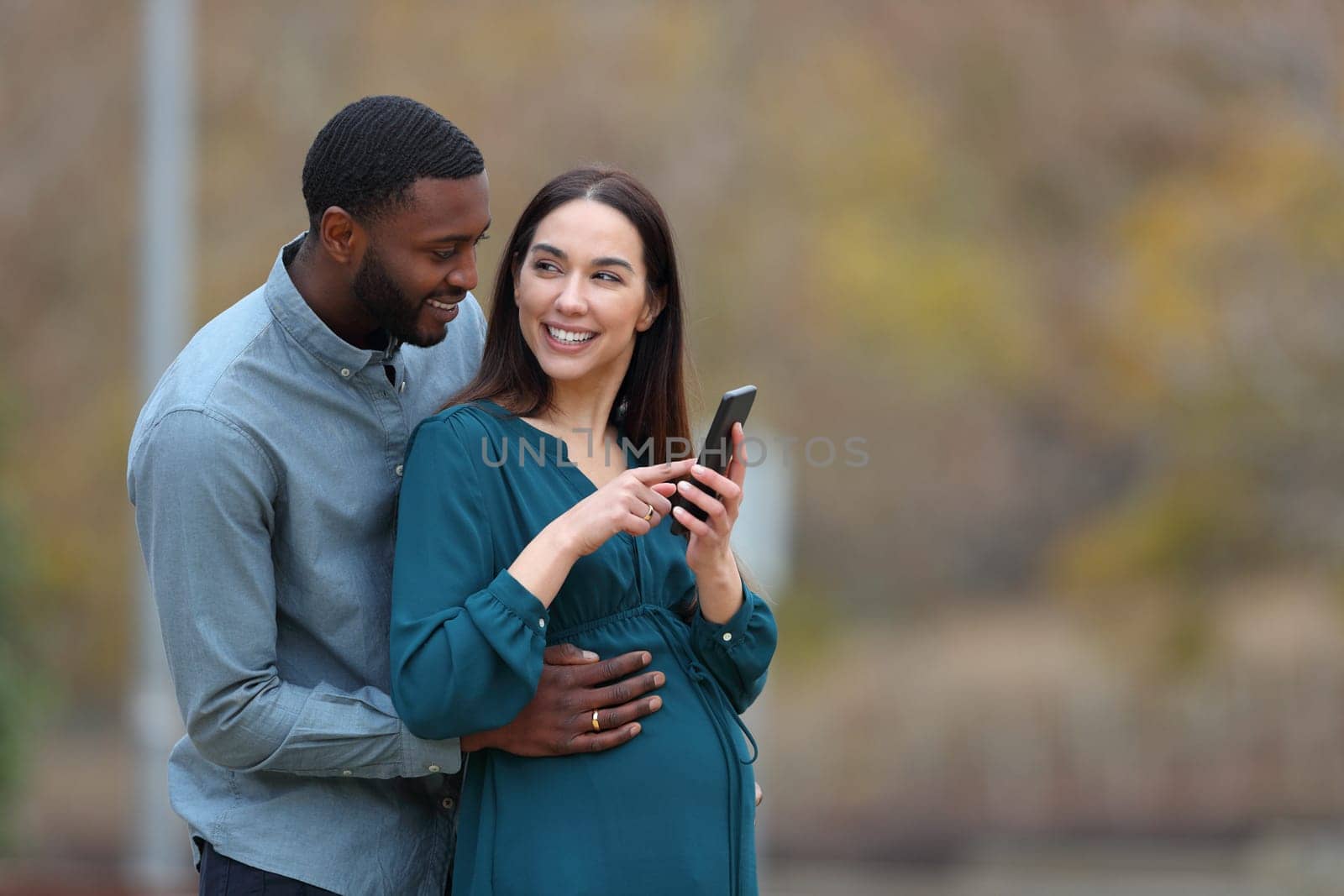 Interracial couple enjoying pregnancy holding phone