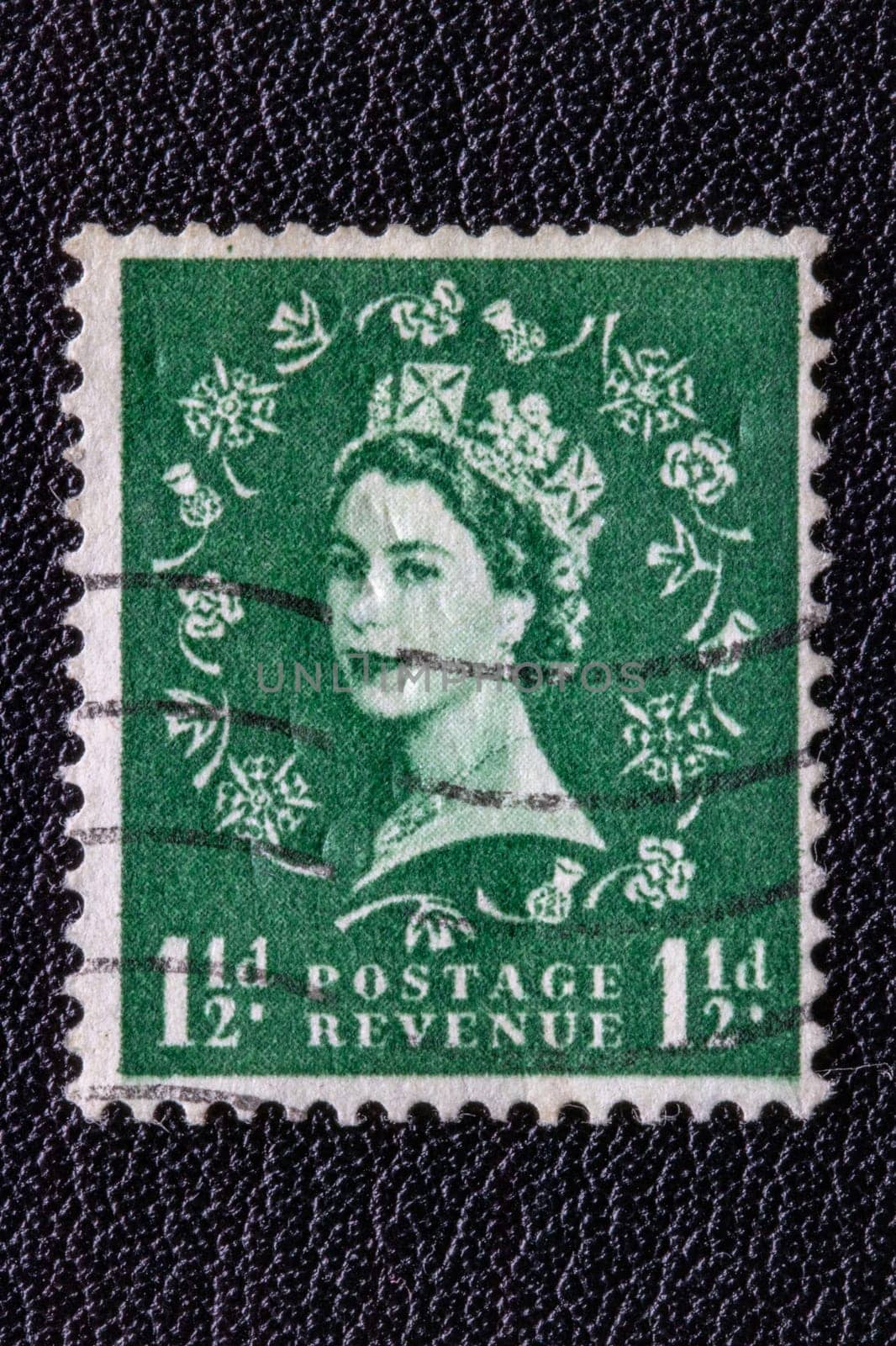 Potsdam, Germany - APR 26, 2022. A old of Great Britain (United Kingdom) issued stamp with portrait of Queen Elizabeth II with postmark on a black leather background. Stamp 1 1/2p, green. Ca. 1952.