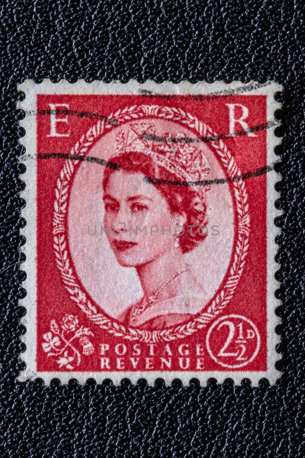 Potsdam, Germany - APR 26, 2022. A old of Great Britain (United Kingdom) issued stamp with portrait of Queen Elizabeth II with postmark on a black leather background. Stamp 2 1/2p, Scarlet. Ca. 1952
