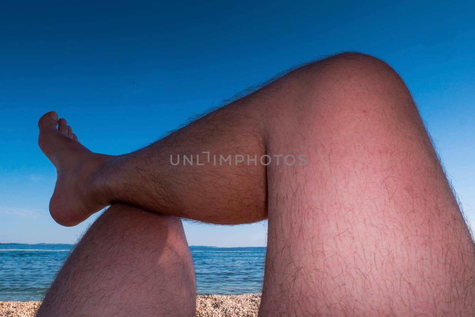 Man's legs are sunbathing on a beach. Point of view.