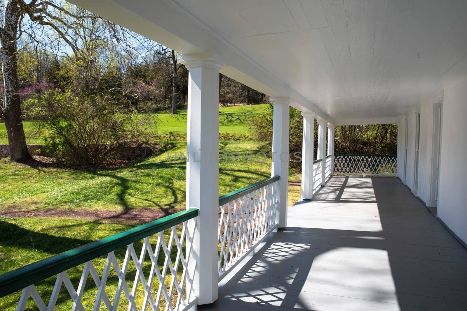 Light and shadows create a dramatic effect in this image shot down the length of the front porch of a colonial american Pennsylvania home. Green grass nature background with sunlight and long shadow lines creating beautiful patterns and geometric shapes. No people, with copy space.