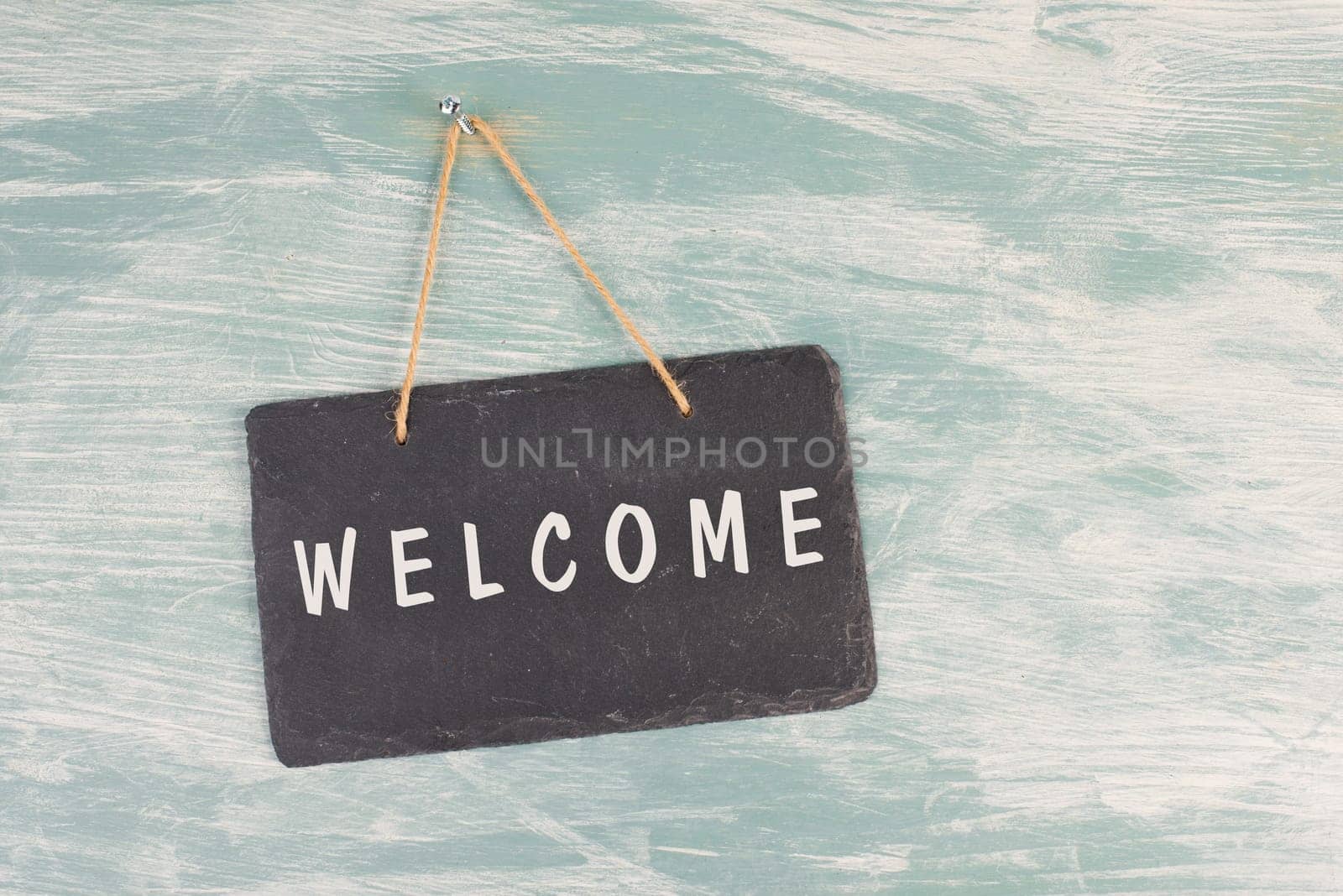 The word welcome is standing on a chalkboard sign, hanging on a blue textured weathered door, greeting to visiter