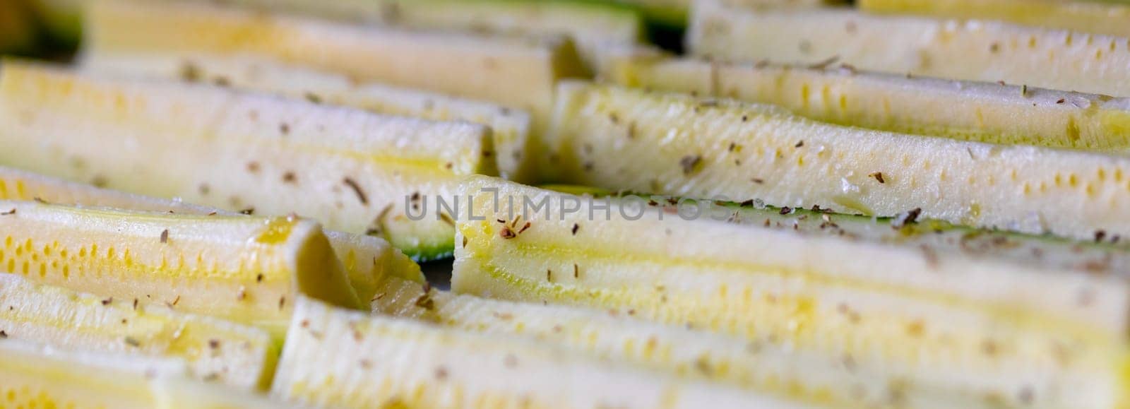 Panorama banner of fresh seasoned zucchini slices or courgettes ready for oven roasting sprinkled with aromatic herbs in a low angle full frame view
