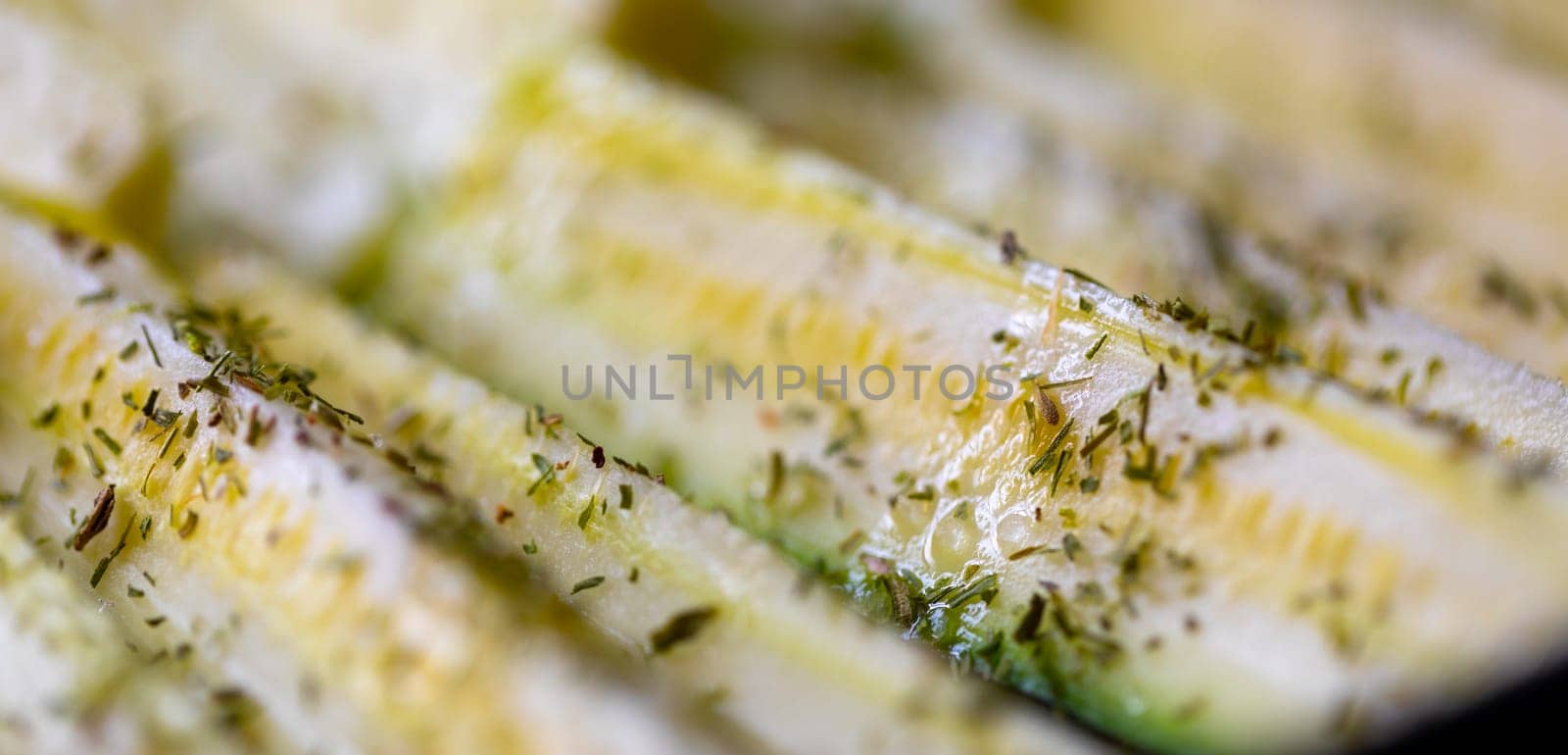 Sliced fresh zucchini seasoned with herbs in a close up view with selective focus to the seasoning in a food cooking concept