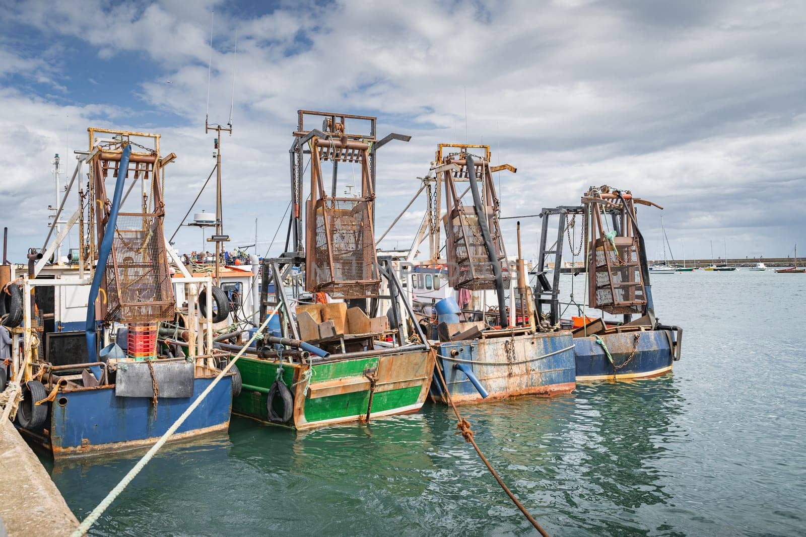Four small fishing boats with shellfish cages moored in Howth harbour. Phishing and shellfish fishing equipment on fishing boats, Dublin, Ireland