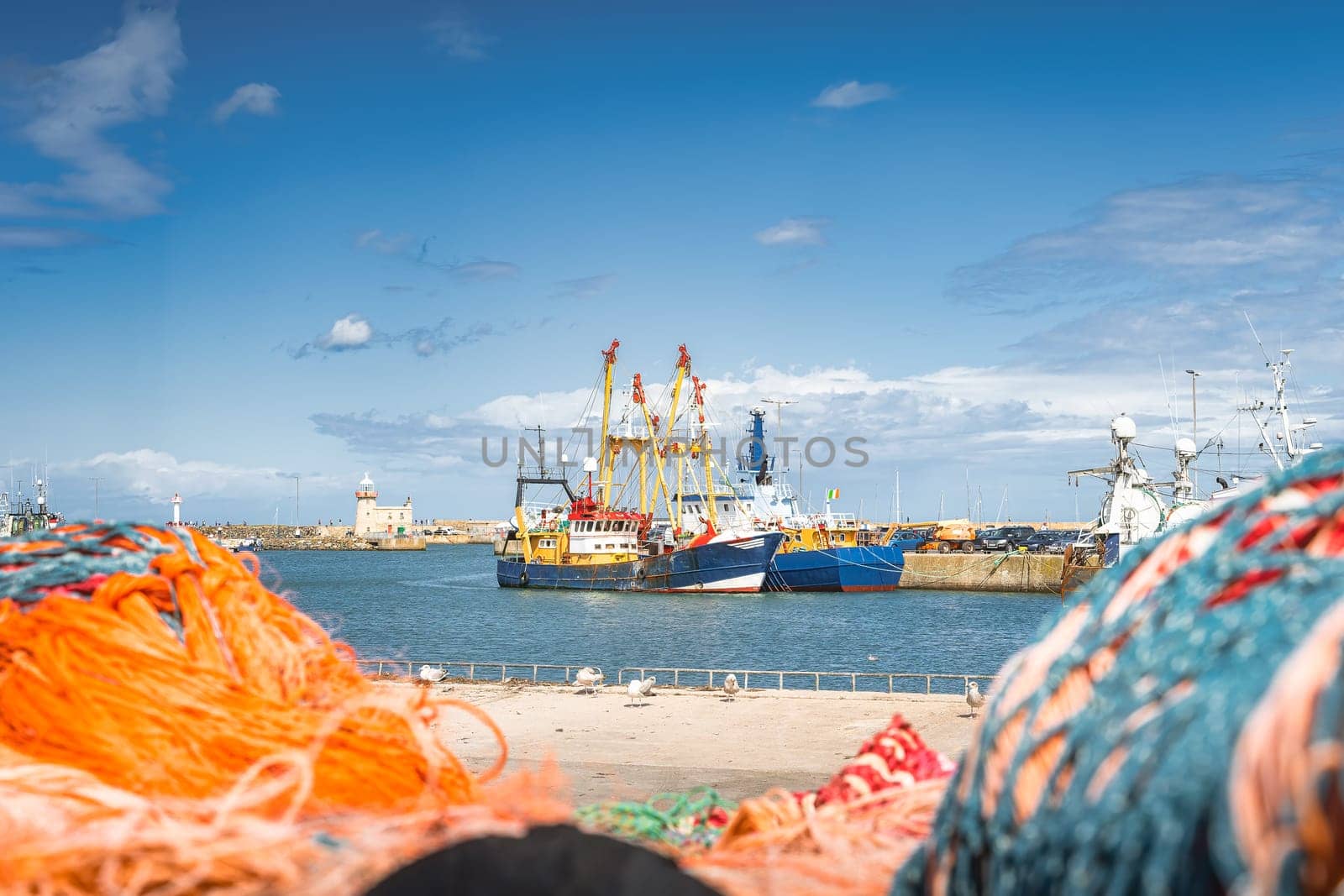 Large fishing boats moored in Howth harbour seen through blurred nets. Phishing and shellfish fishing equipment on fishing boats, Dublin, Ireland