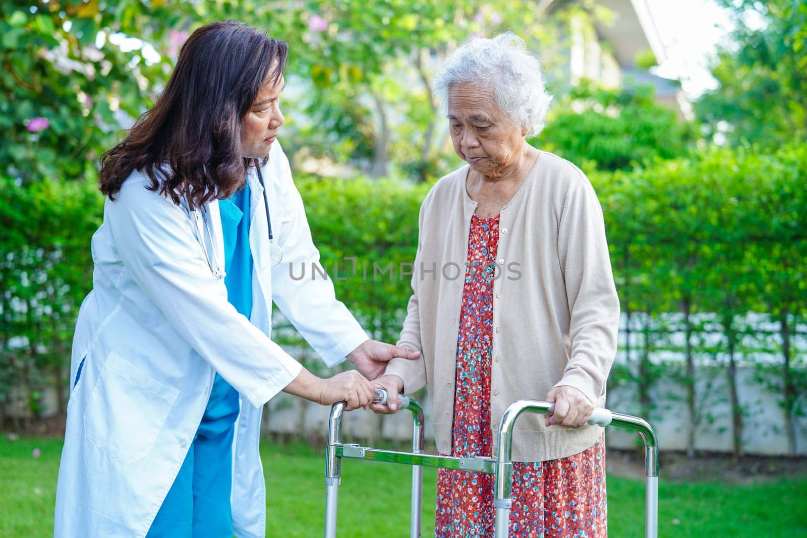 Doctor help Asian elderly woman disability patient walk with walker in nursing hospital, medical concept.