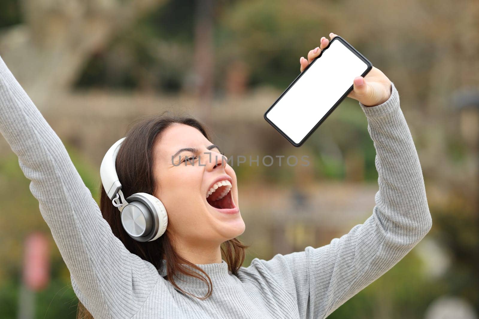 Happy teen singing showing phone screen in a park