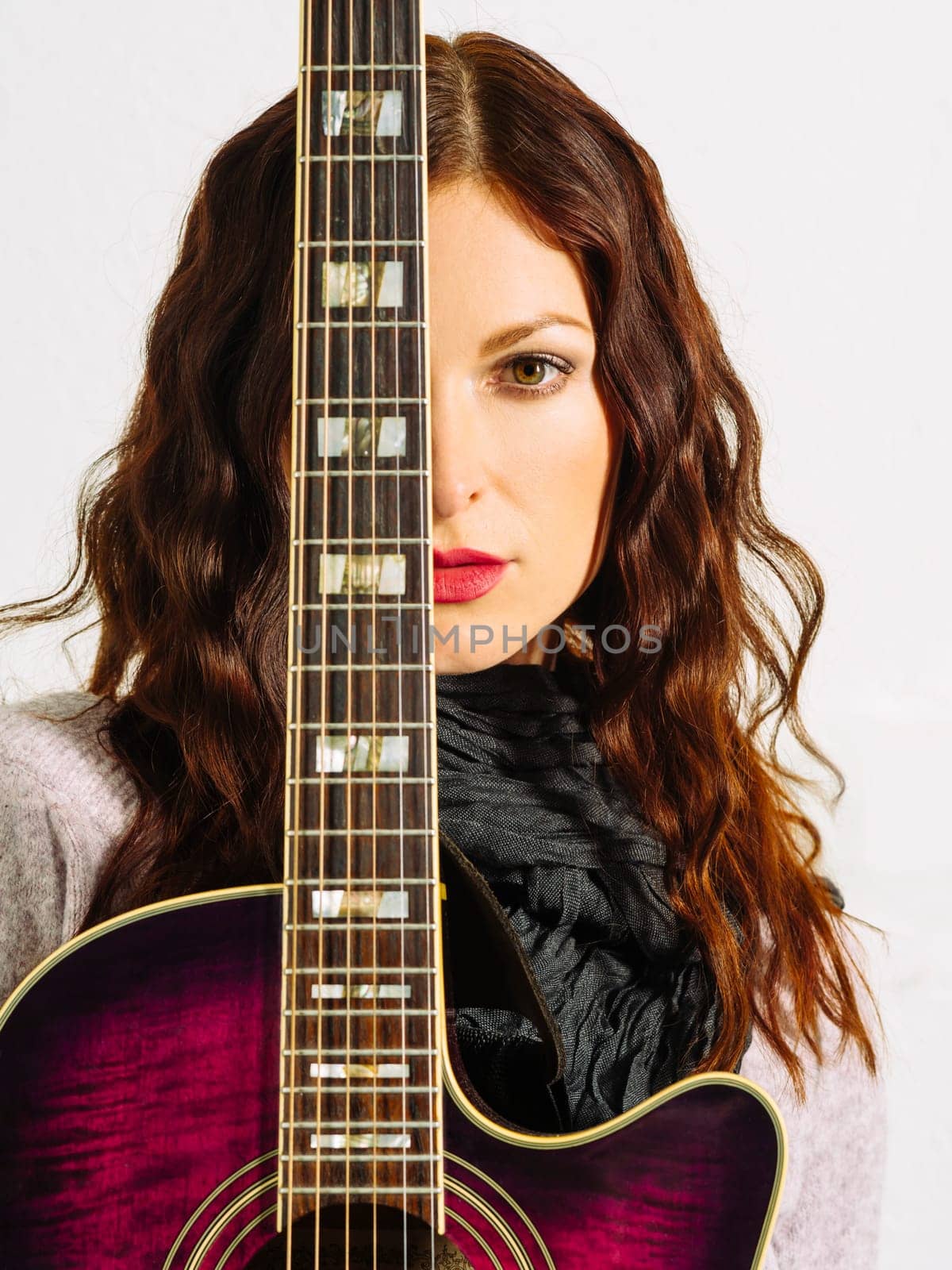 Young beautiful redhead woman holding an acoustic guitar over her face.