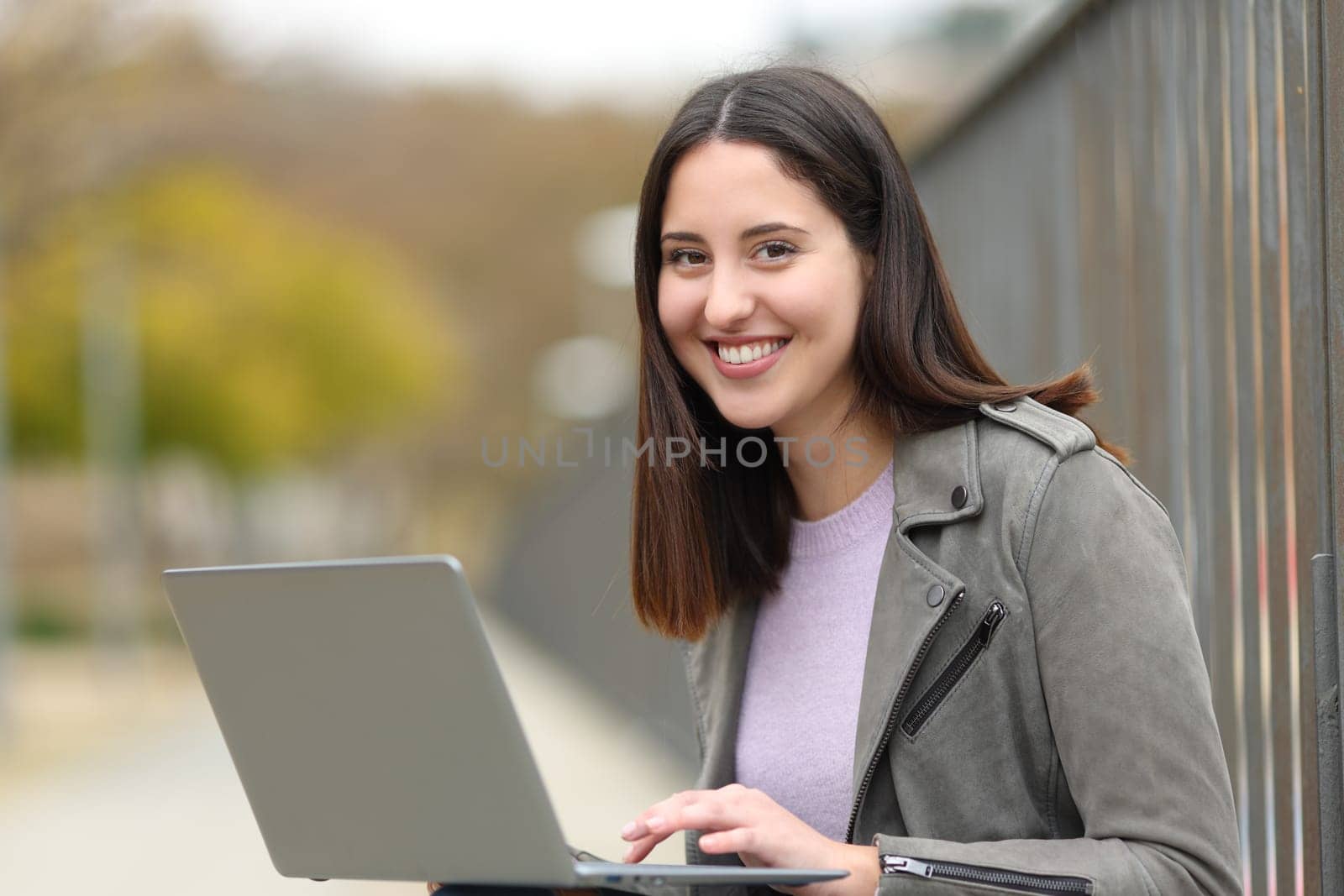 Happy woman using laptop in the street looking at you