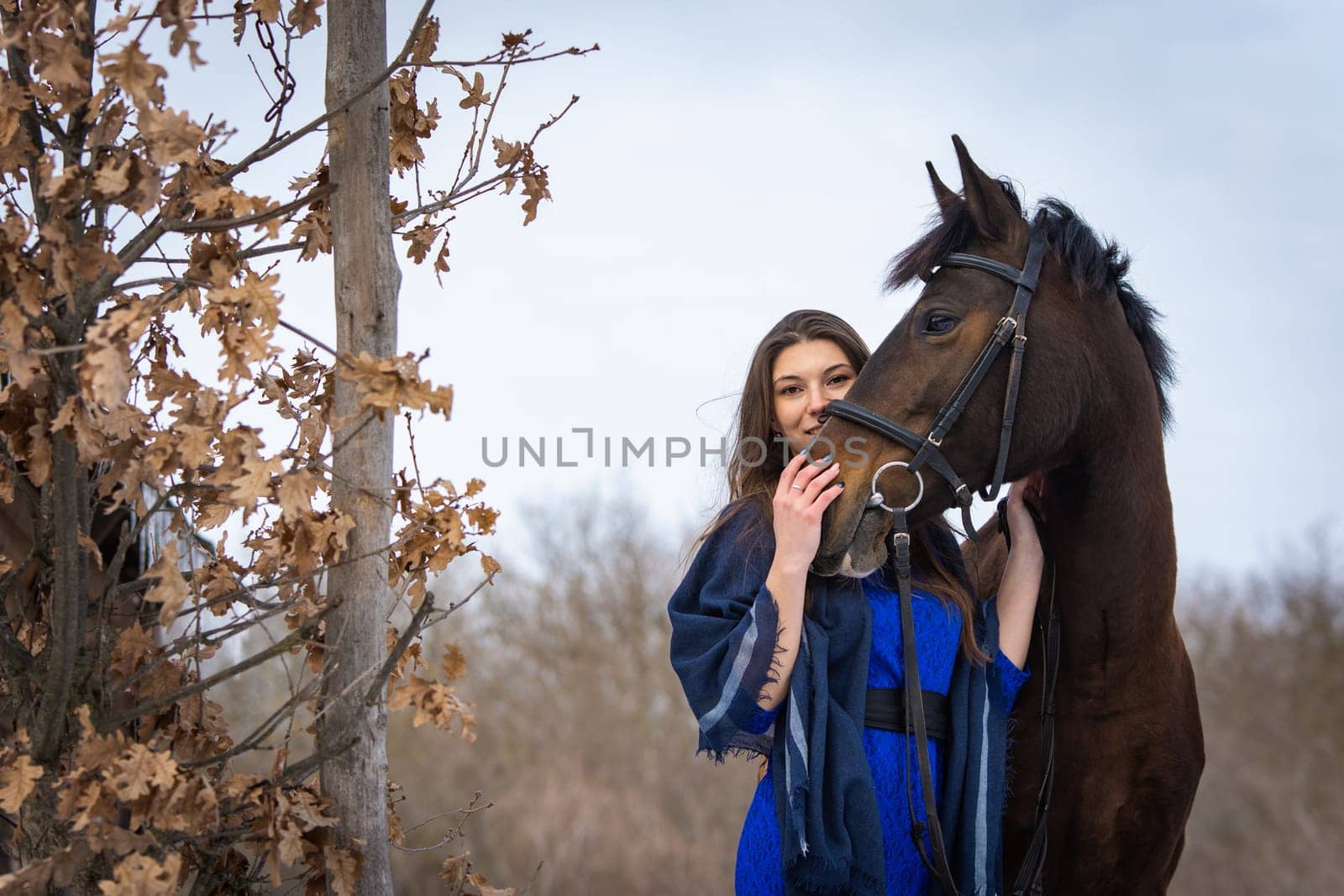 The girl peeks out from behind the muzzle of a horse, in the background an autumn forest