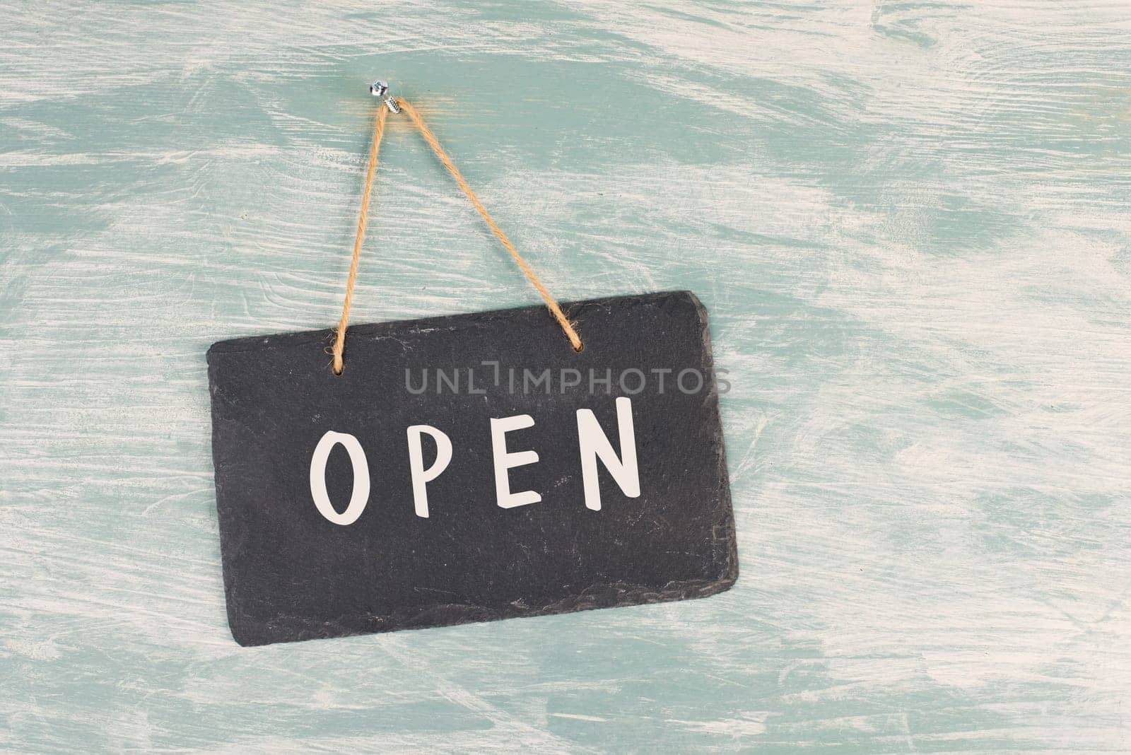 The word open is standing on a chalkboard sign, hanging on a blue textured weathered door, concept for business, stores and restaurants
