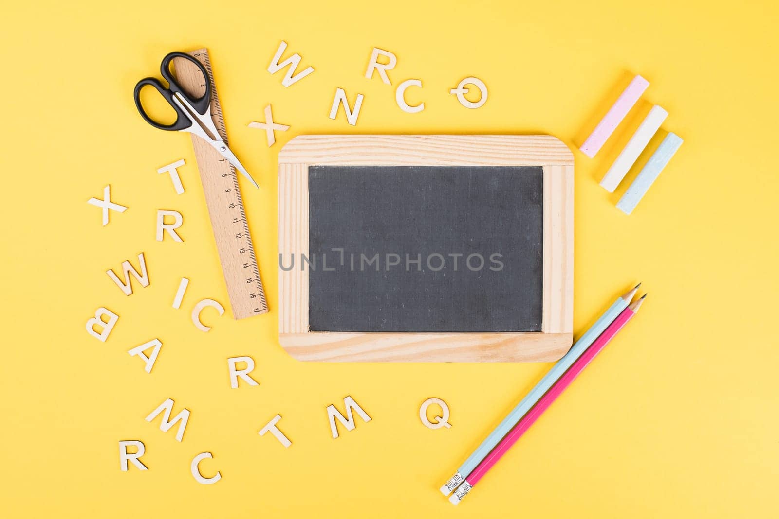 Empty chalkboard with colorful chalk, pencils, ruler, letters and a scissor, back to school and education concept