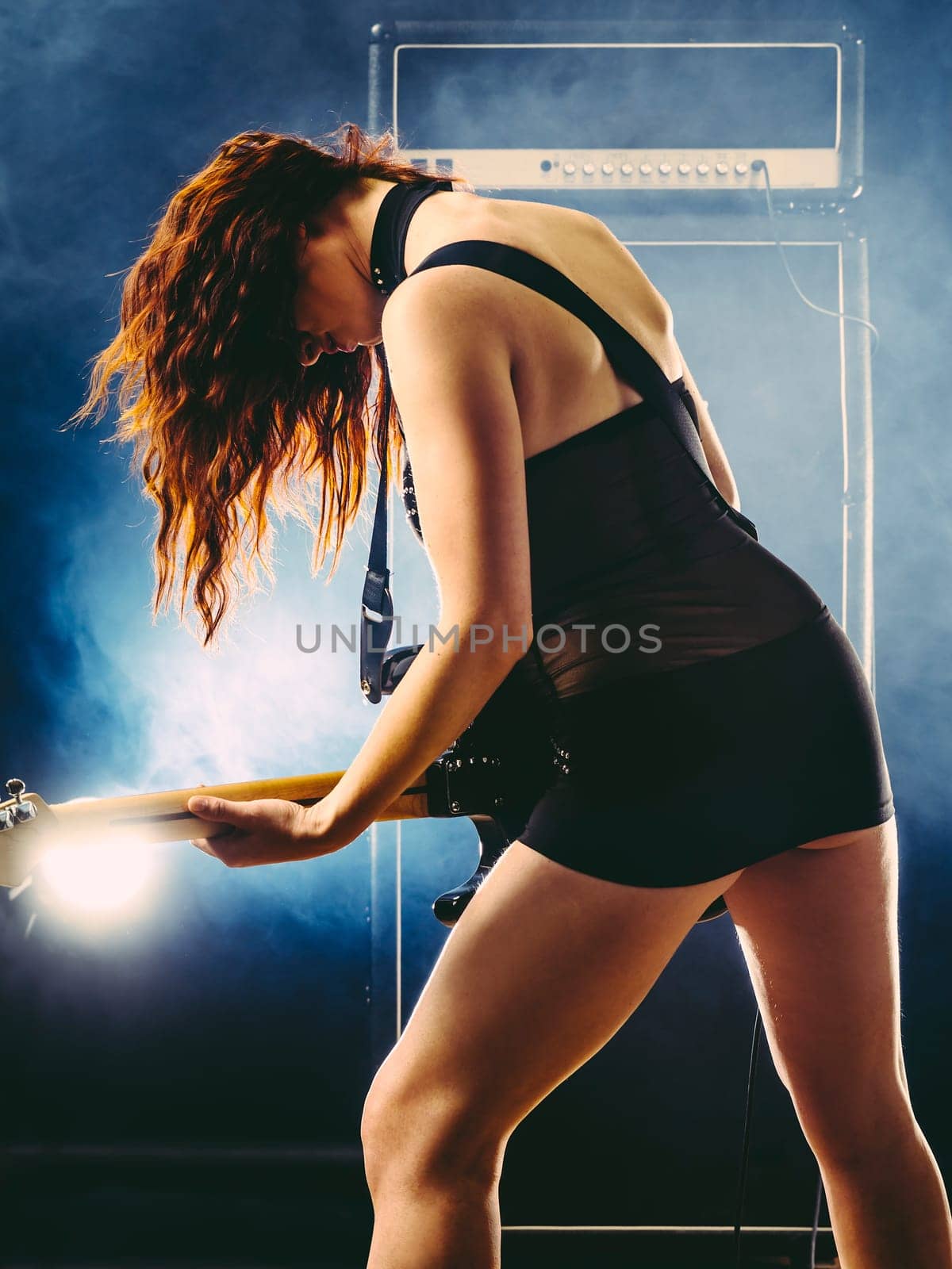 Young beautiful woman playing an electric guitar in front of large amplifier.