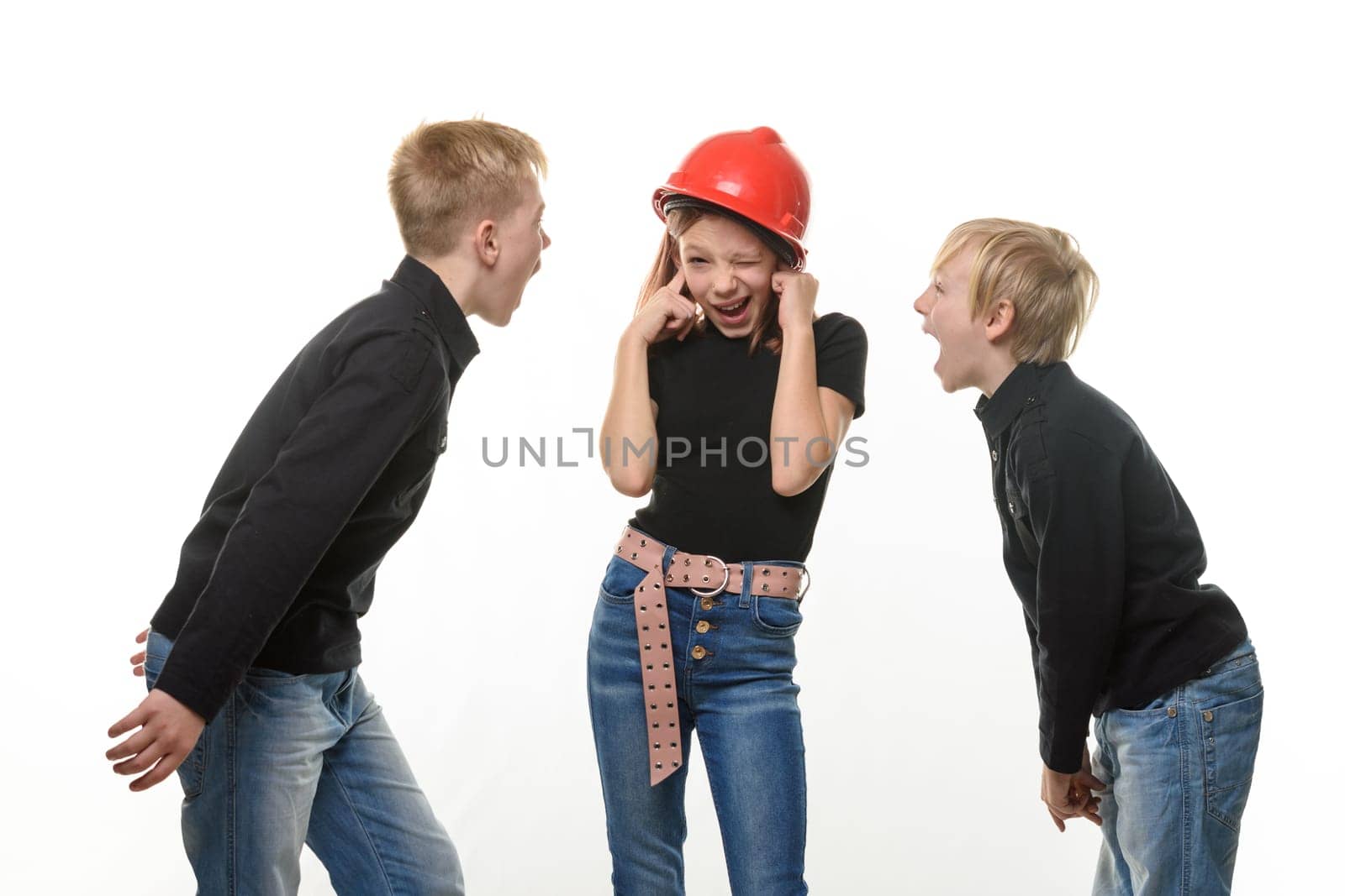 Two boys are shouting at a girl, the girl is standing in a helmet in a helmet and plugged her ears